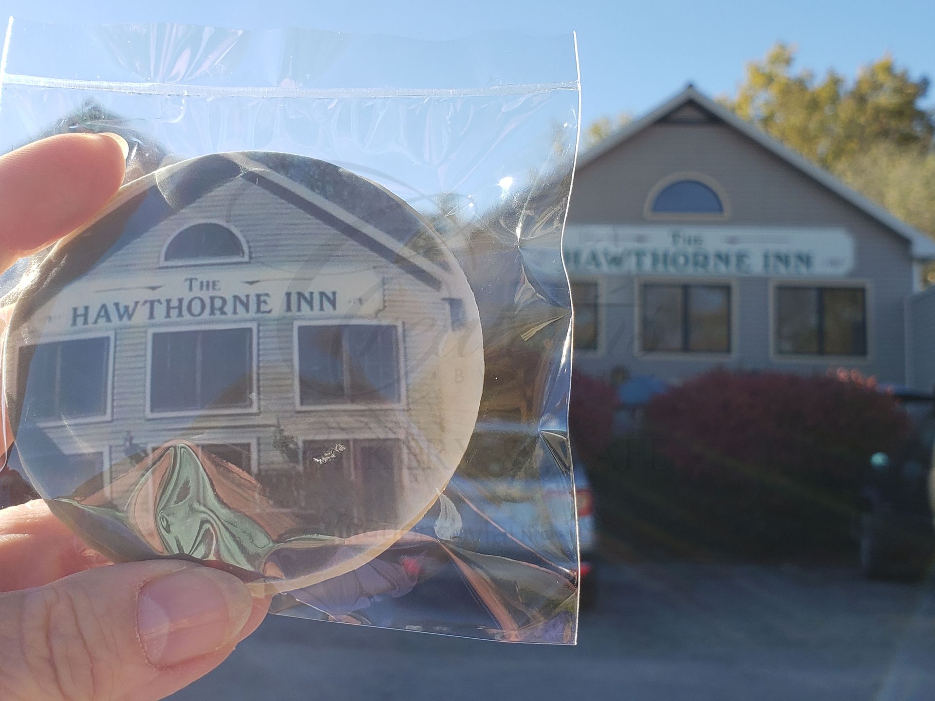 Hand holding a Hawthorne Inn keychain in front of the Hawthorne Inn building sign.