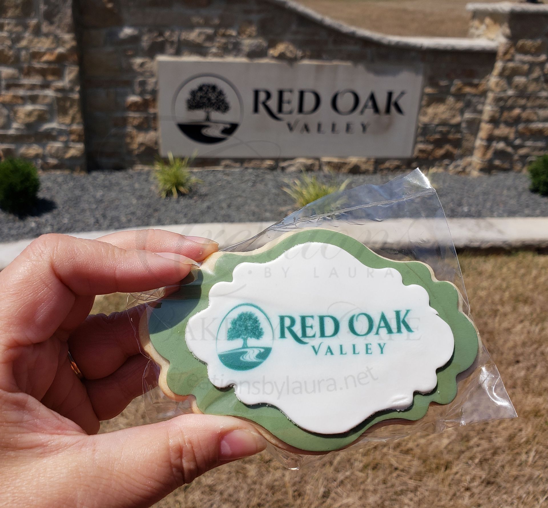 Hand holding a green Red Oak Valley sticker in front of a Red Oak Valley sign.