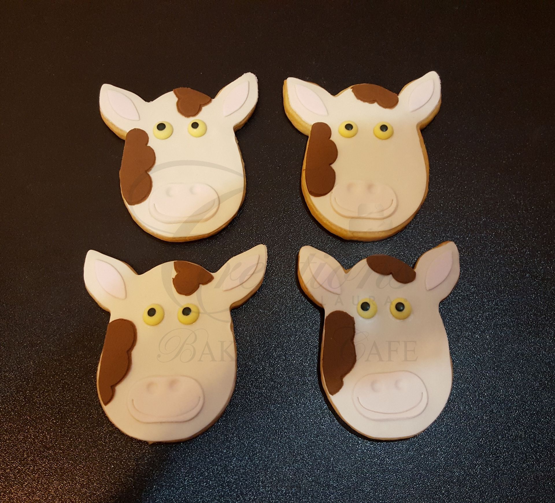 Four cow-face cookies with white frosting and brown spots on a dark surface
