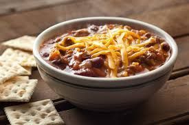 a bowl of chili with cheese and crackers on a wooden table