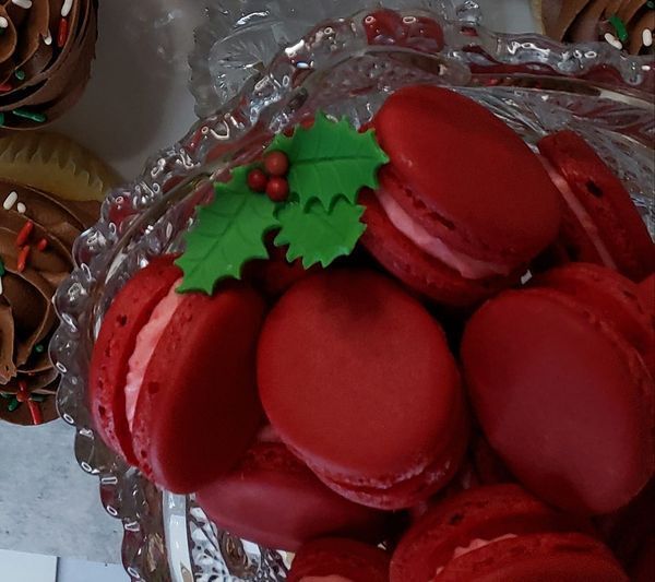 A glass bowl filled with red macarons with a holly leaf on top