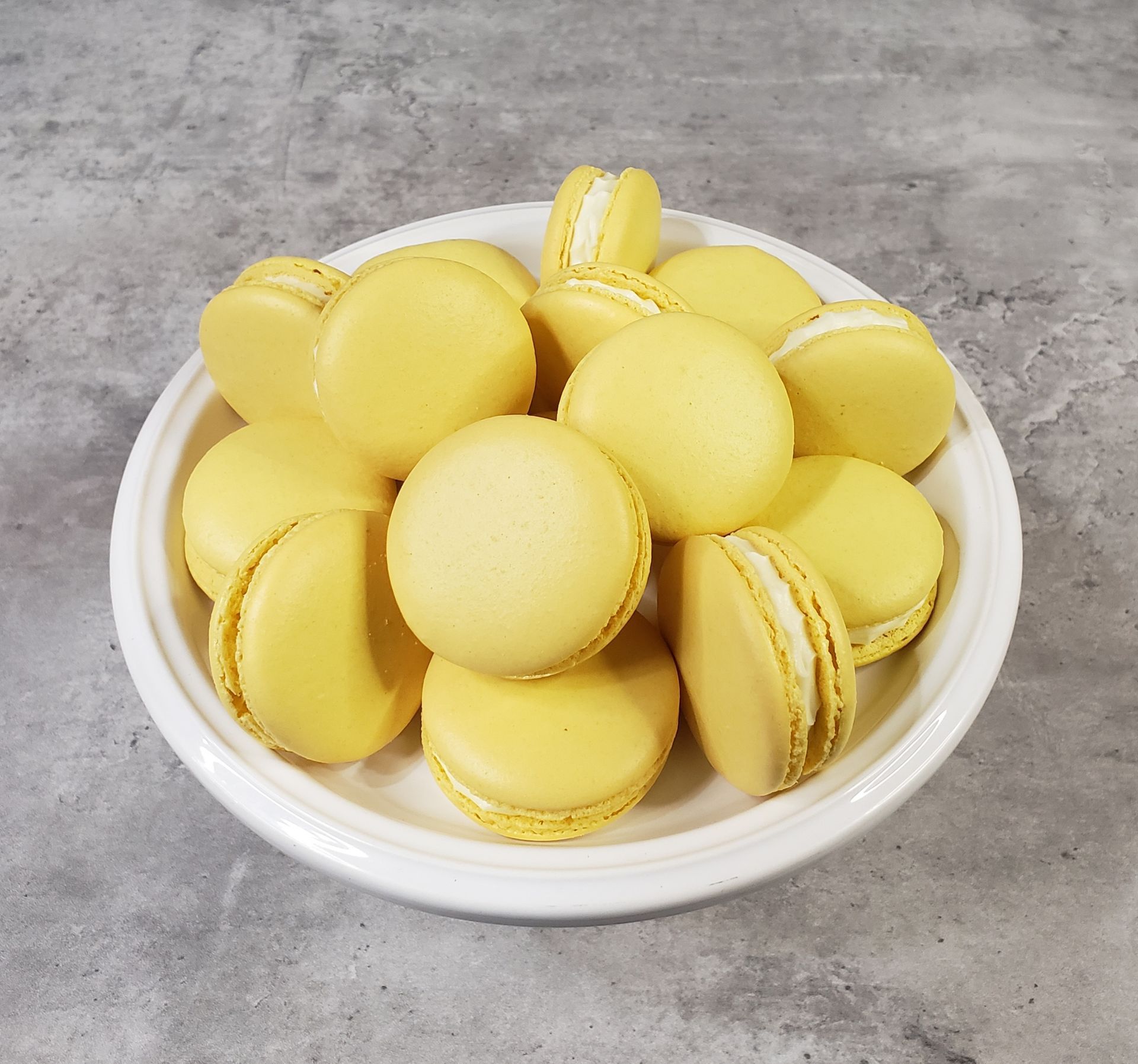 A white bowl filled with yellow macarons on a table.