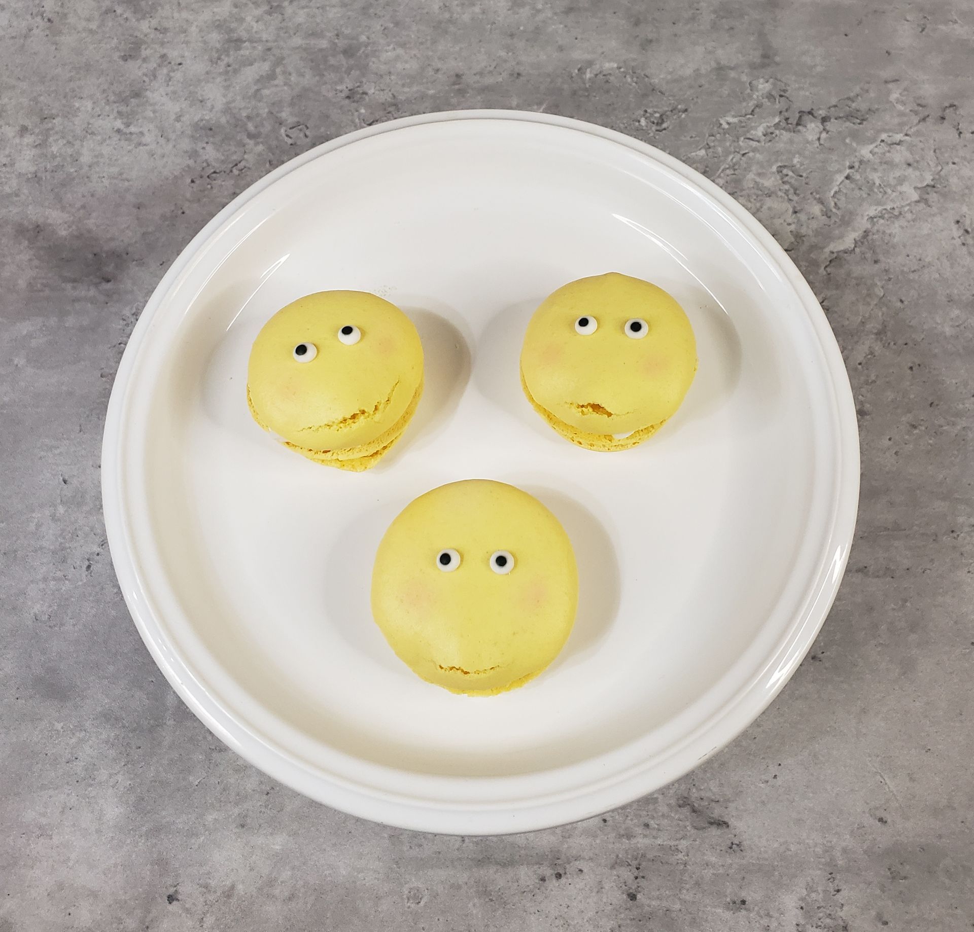 Three yellow macarons with eyes on them on a white plate