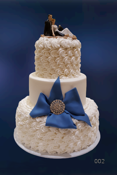 Two-tier white wedding cake with blue ribbon flower and bride-and-groom topper