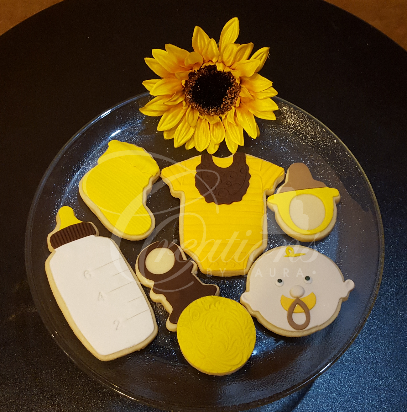 A plate of baby shower cookies with a sunflower in the background