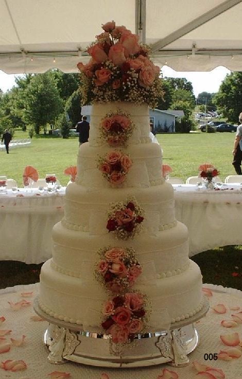 Five-tier white wedding cake with pink floral decorations under a tent