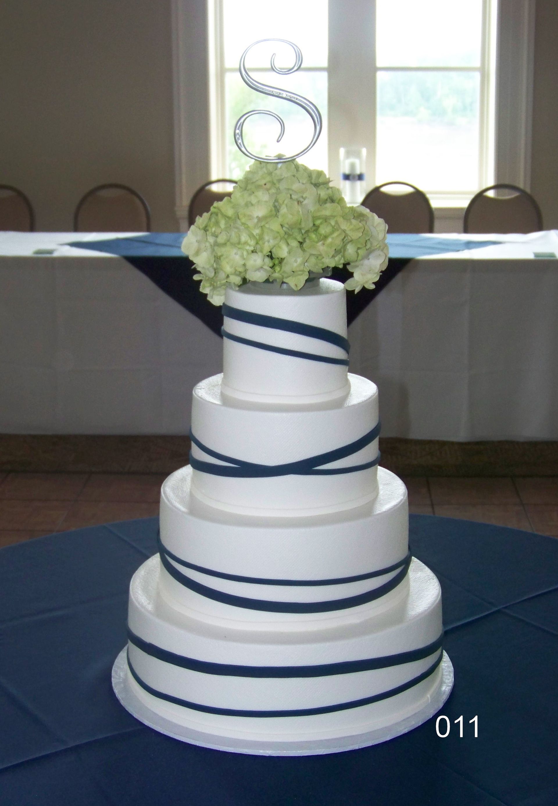 White tiered wedding cake with blue ribbon accents and white flowers on a table indoors