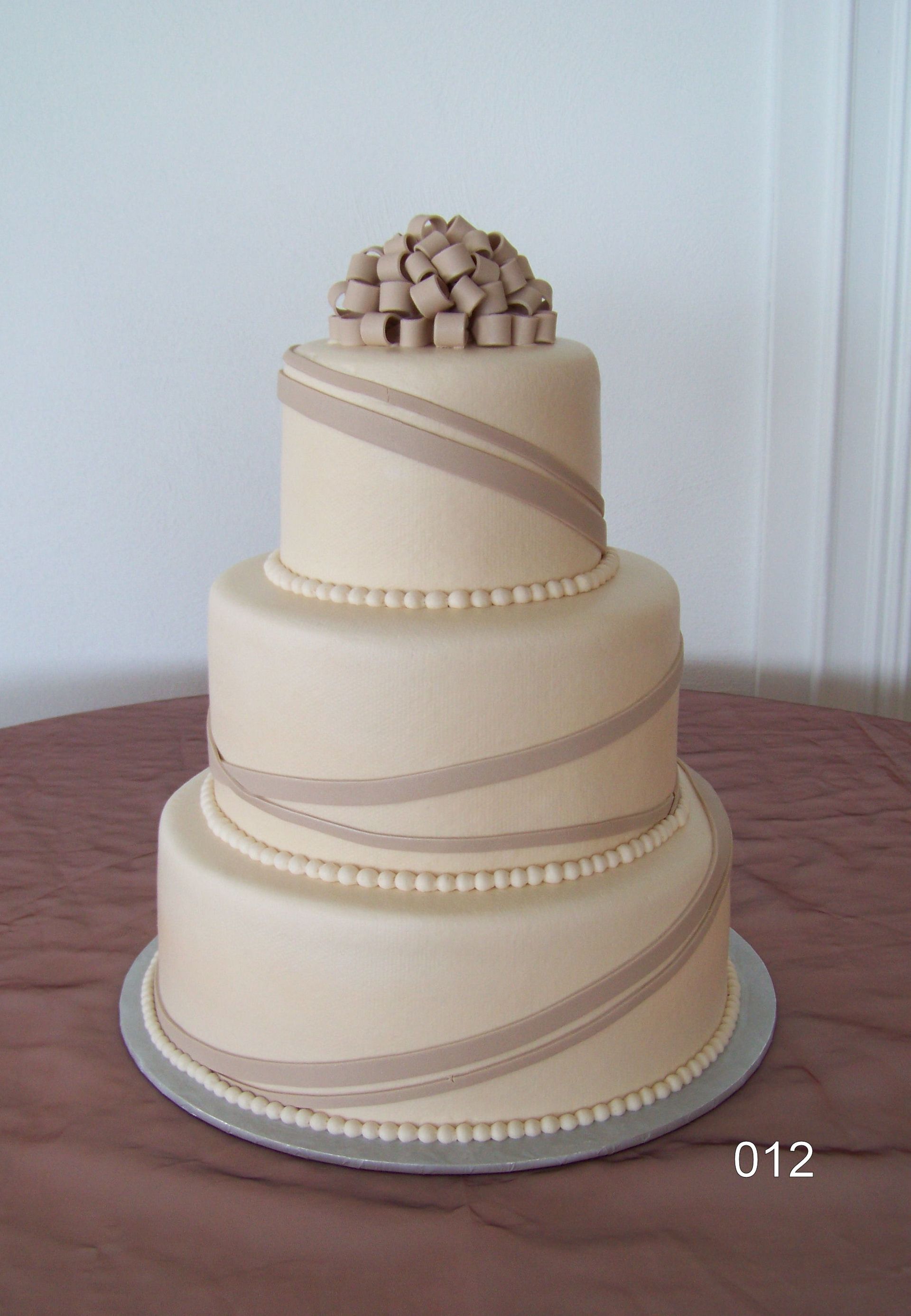 Three-tier beige wedding cake with pearl bands and a cluster of beige flowers on top