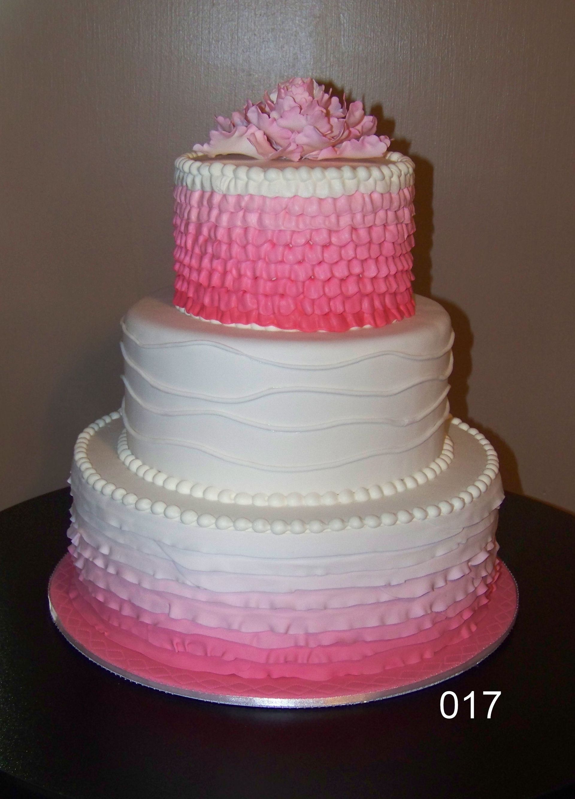 Three-tier white and pink frosted cake with ruffled pink top layer on a plain background