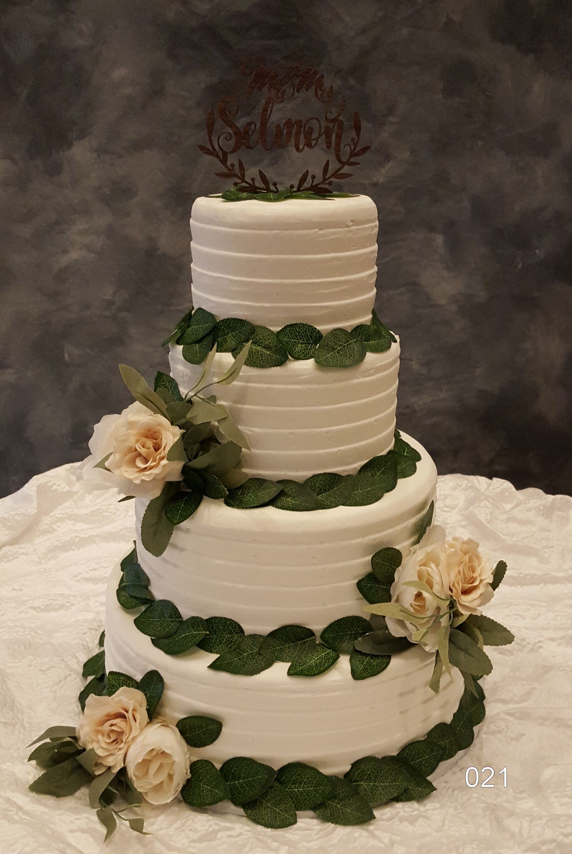 Three-tier white wedding cake with green leaf garlands and cream roses on a lace tablecloth.