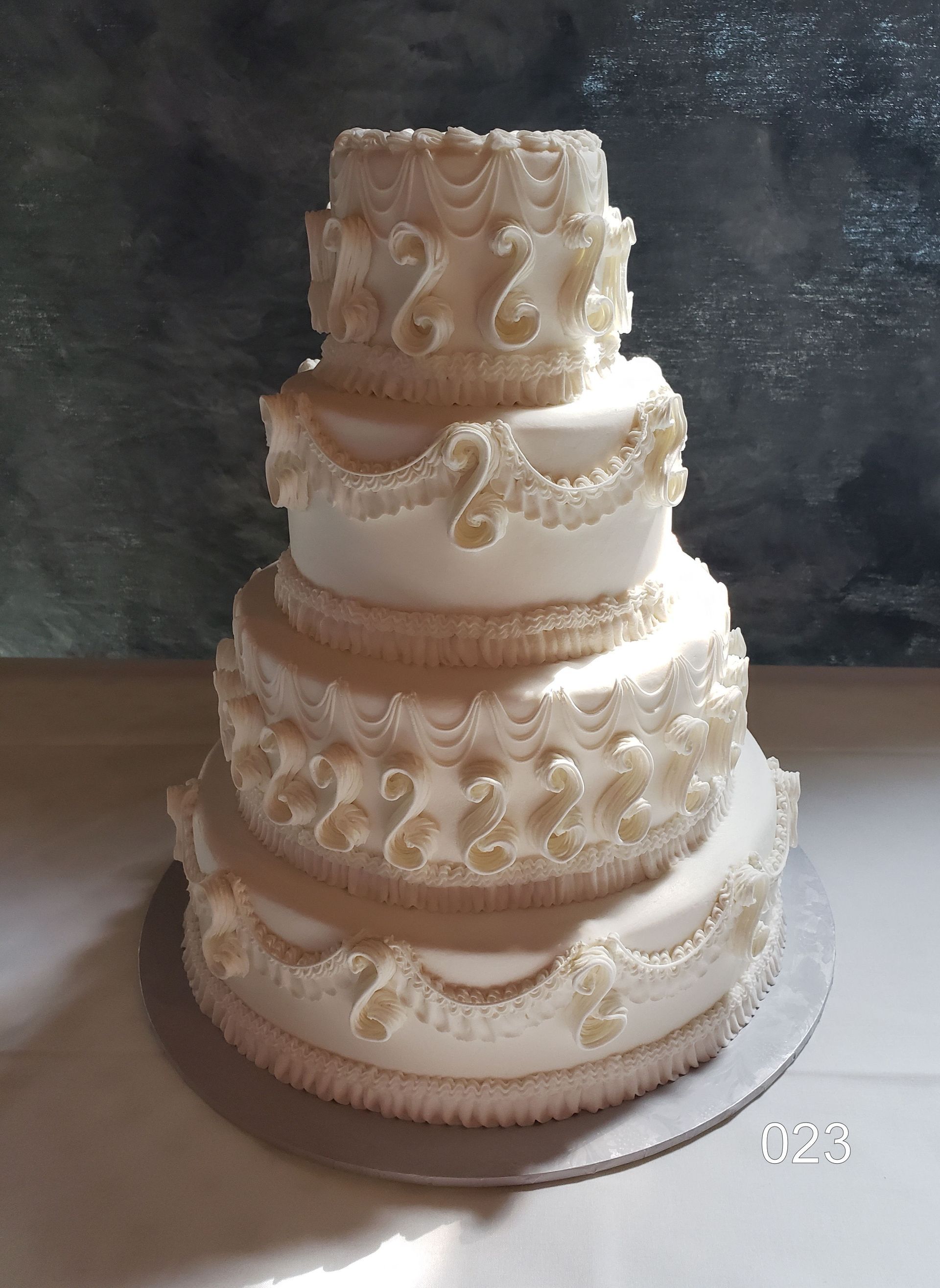 Three-tier white wedding cake with gold bead trim and floral piping on a round cake board