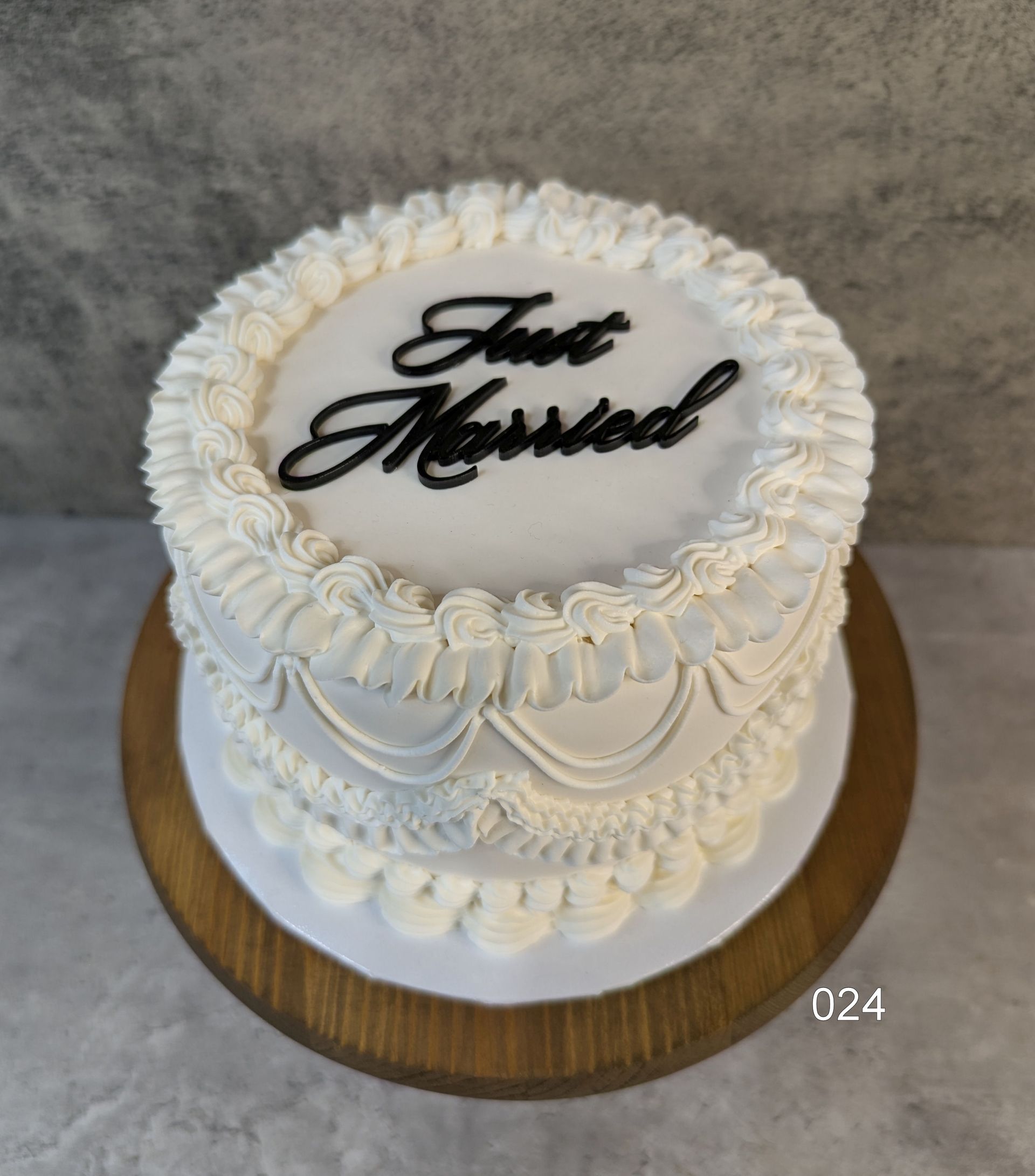 White frosted cake with black “Just Married” topper on a wooden board