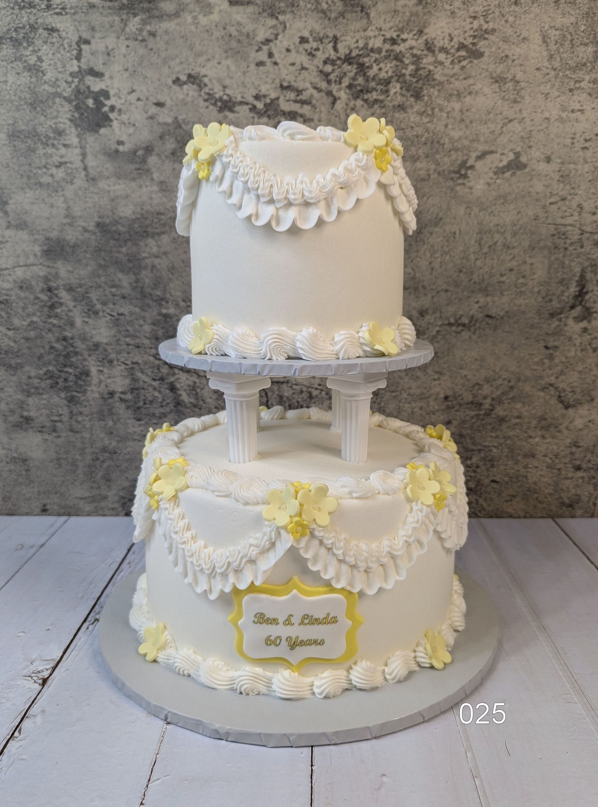 White two-tier wedding cake with yellow flowers and scalloped icing on a round stand