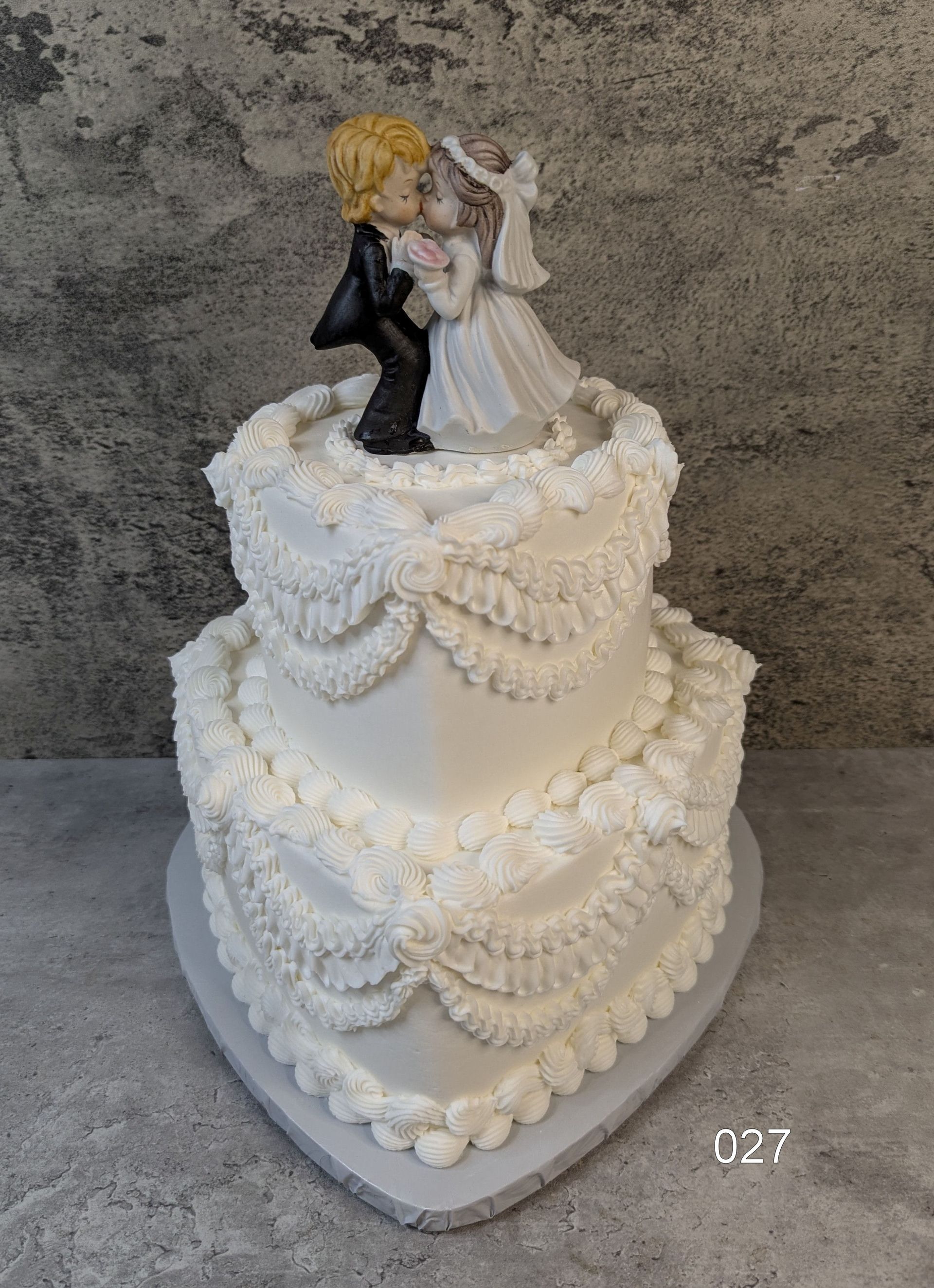 White tiered wedding cake with a bride and groom topper on a gray tabletop