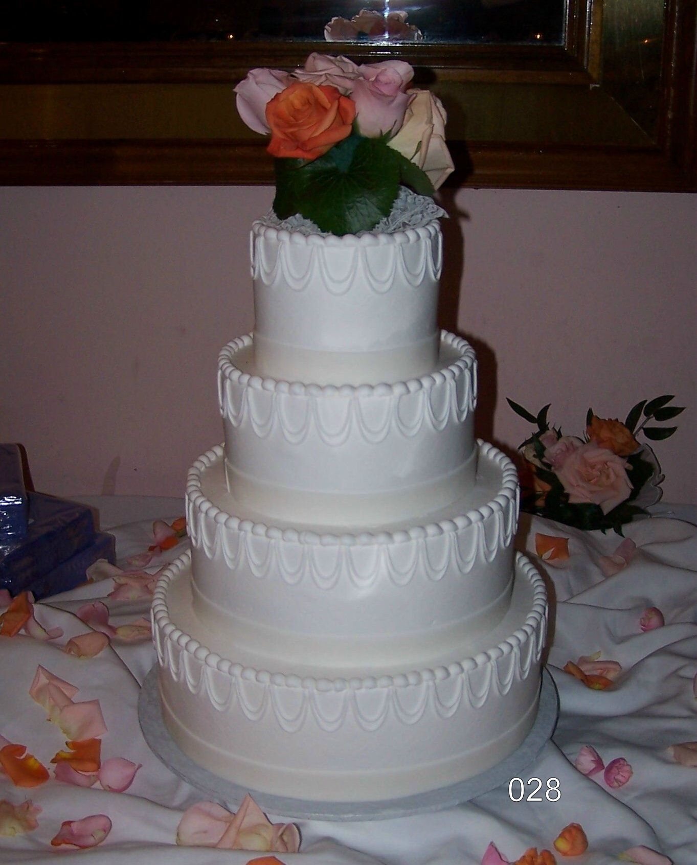 Four-tier white wedding cake with pink and peach roses on top, on a decorated table.