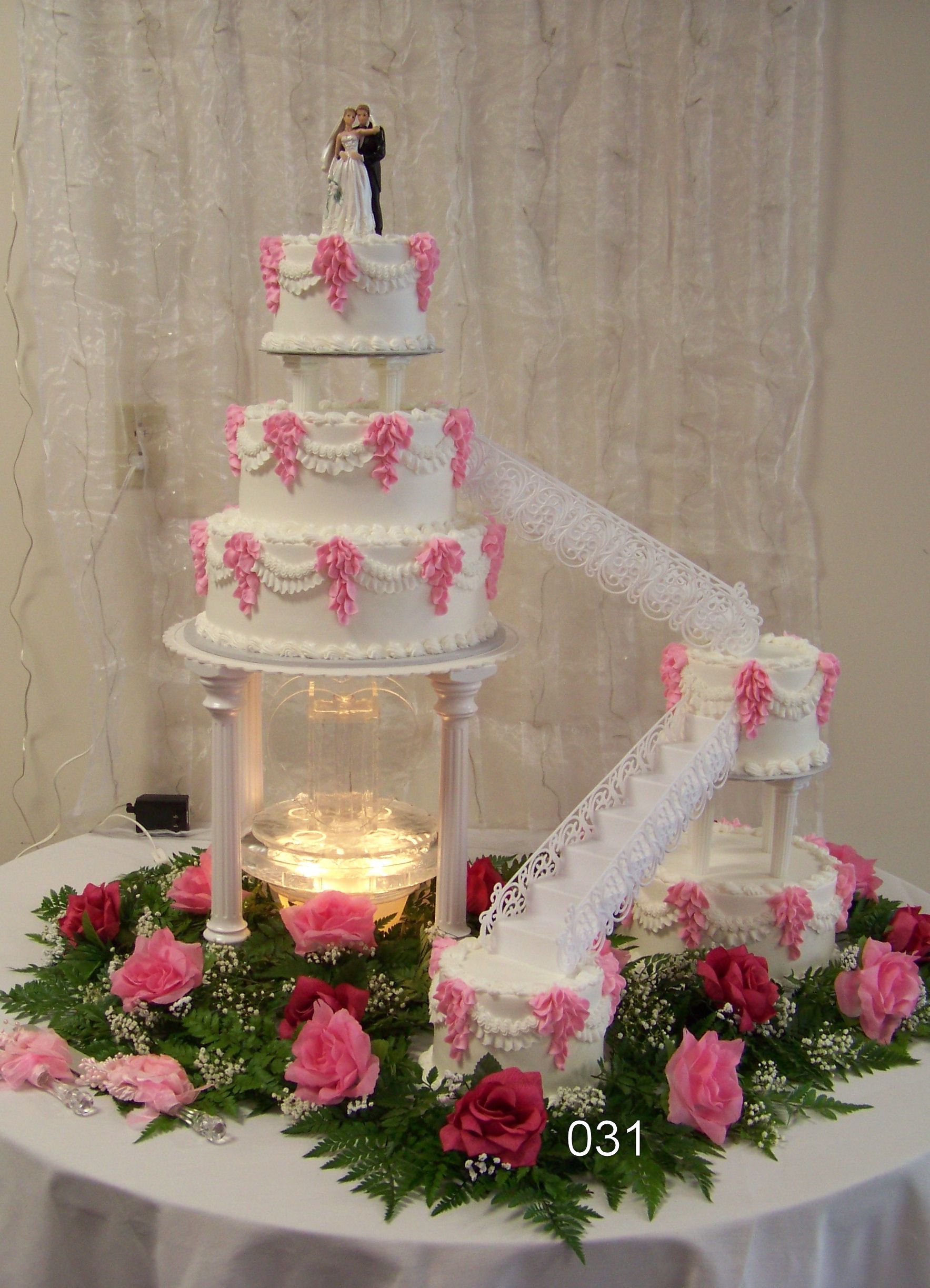 Three-tier pink and white wedding cake with flowers, on a decorated table with candles and ribbon staircase