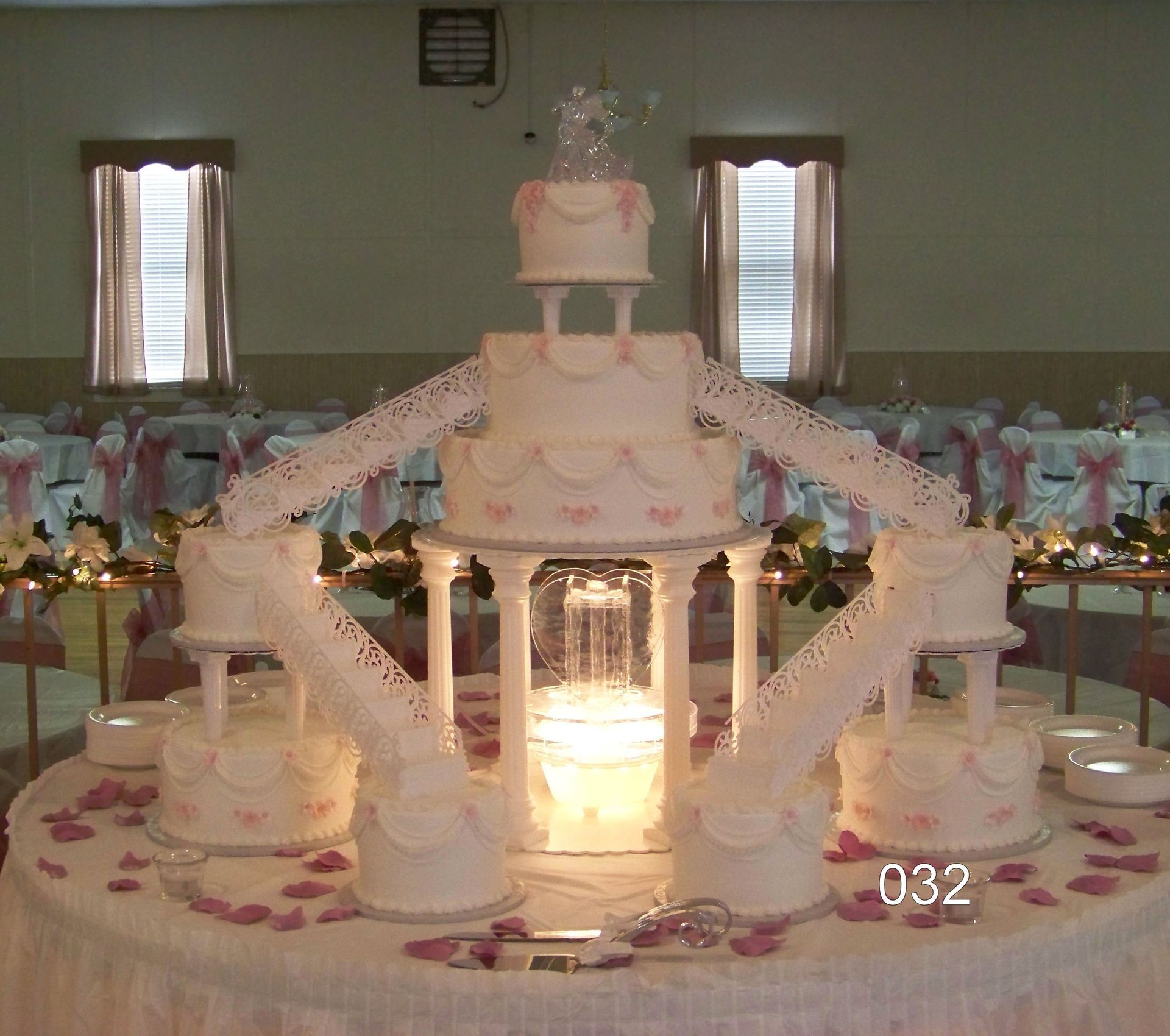 White multi-tiered wedding cake with candle centerpiece and floral decorations on a banquet table