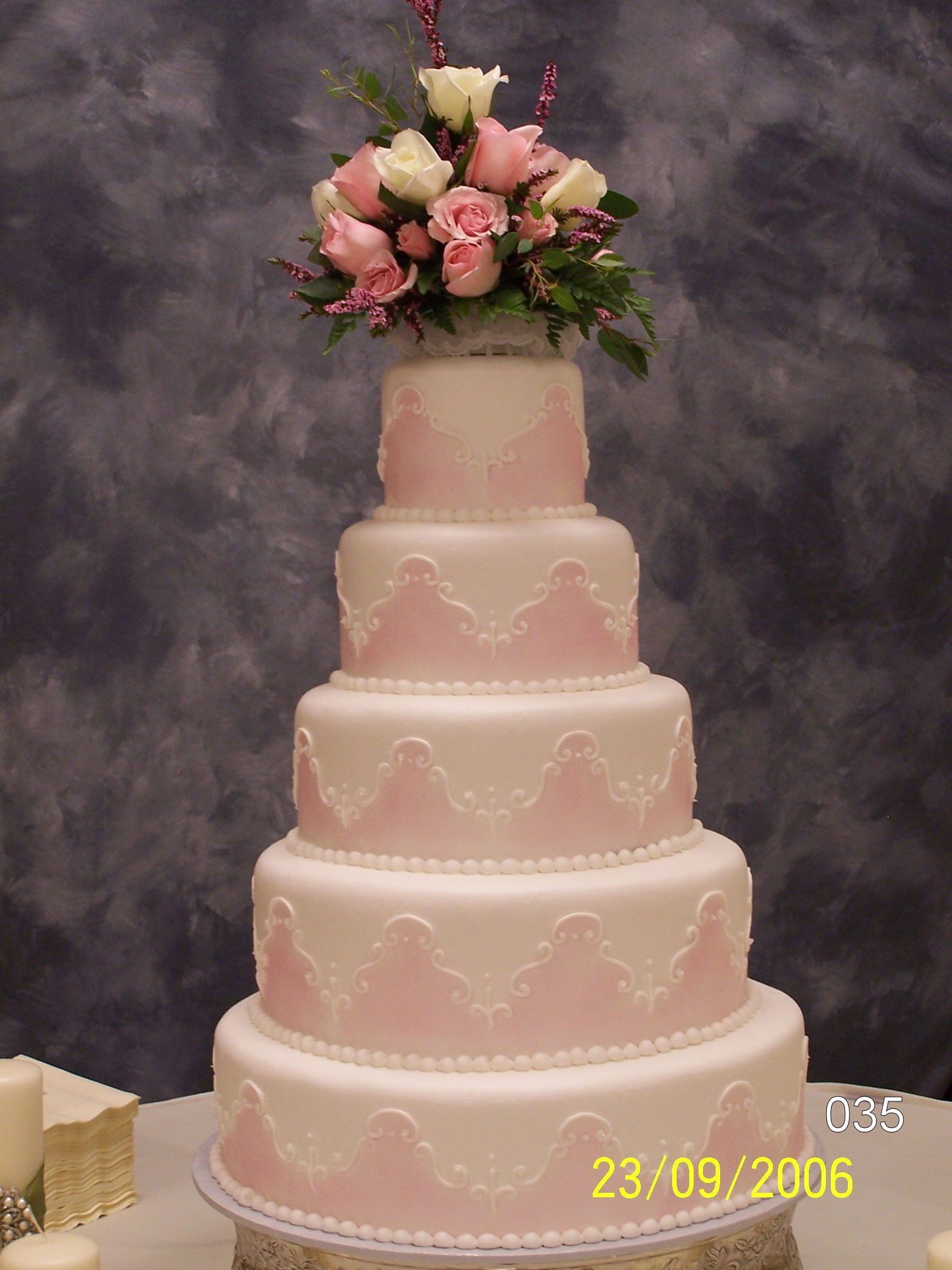Five-tier pink wedding cake topped with pink and white flowers on a gray backdrop