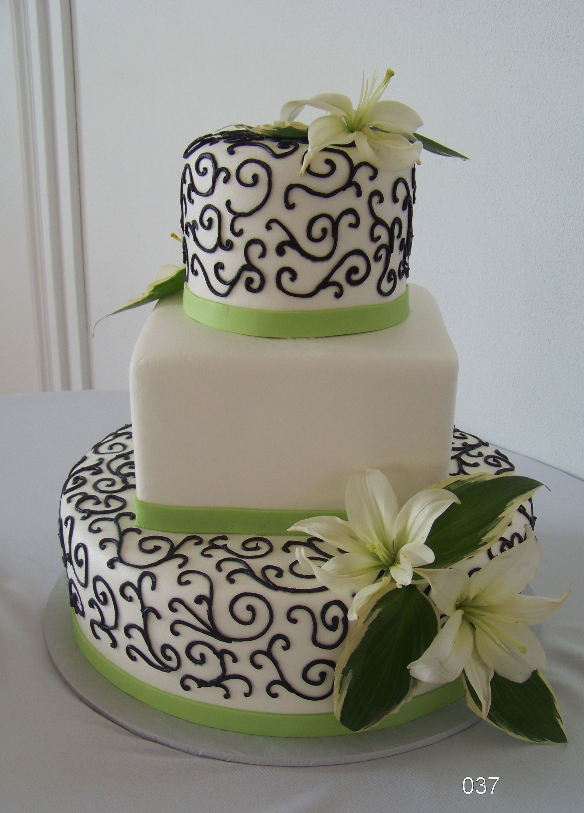 Three-tier white cake with black swirl pattern and white lilies, trimmed with green ribbon