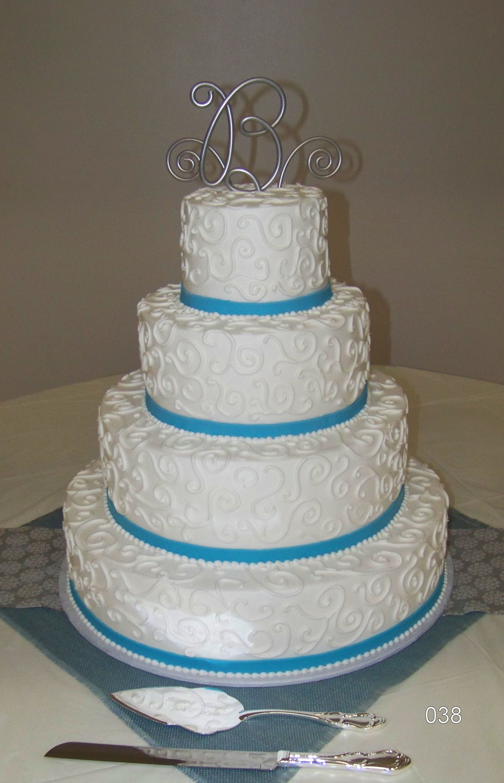 Four-tier white wedding cake with blue ribbon accents and silver monogram topper