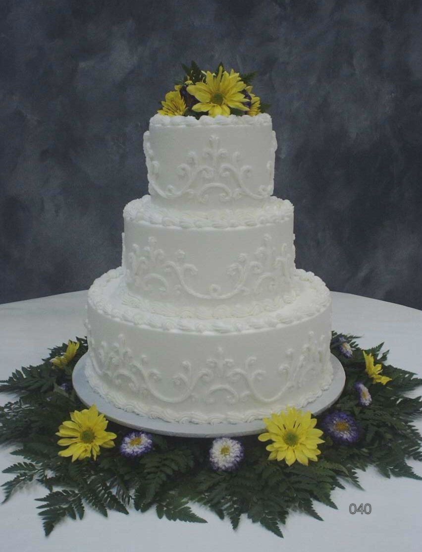 Three-tier white wedding cake with yellow flowers and green foliage on a table