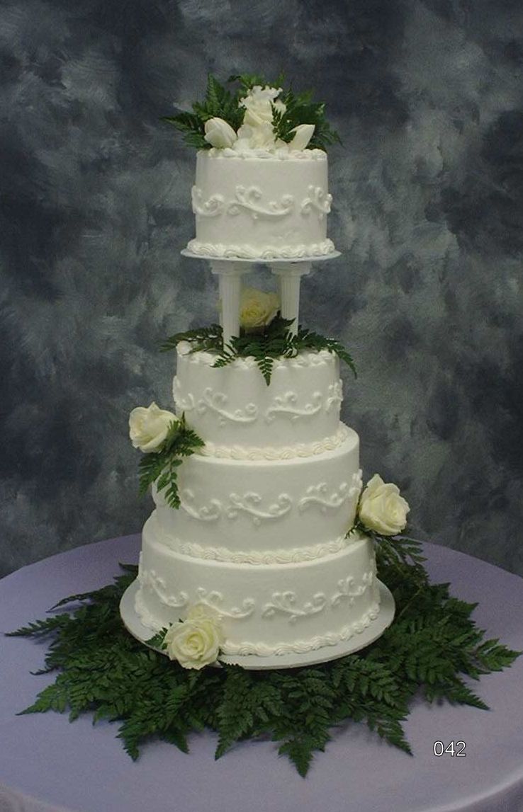 Three-tier white wedding cake with white flowers and greenery on a dark backdrop