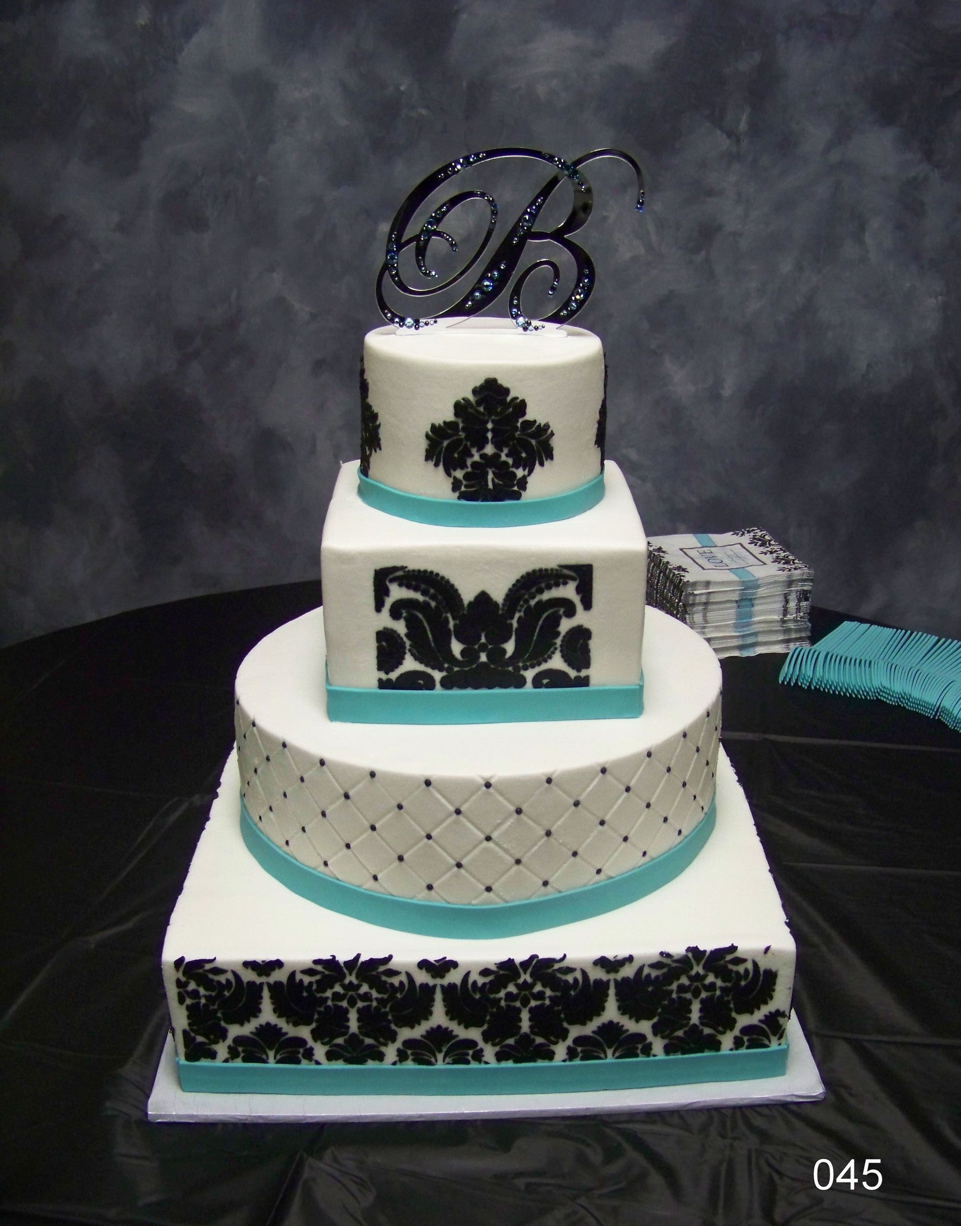 Three-tier white cake with black damask patterns and teal accents on a table.