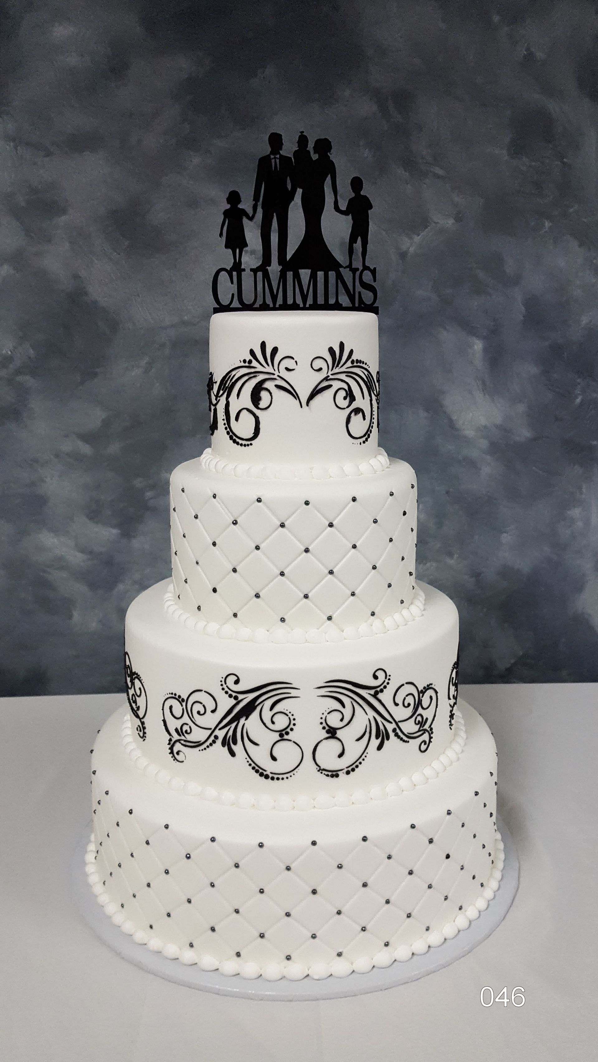 White tiered wedding cake with black silhouette toppers and ornate black scrollwork on a gray backdrop