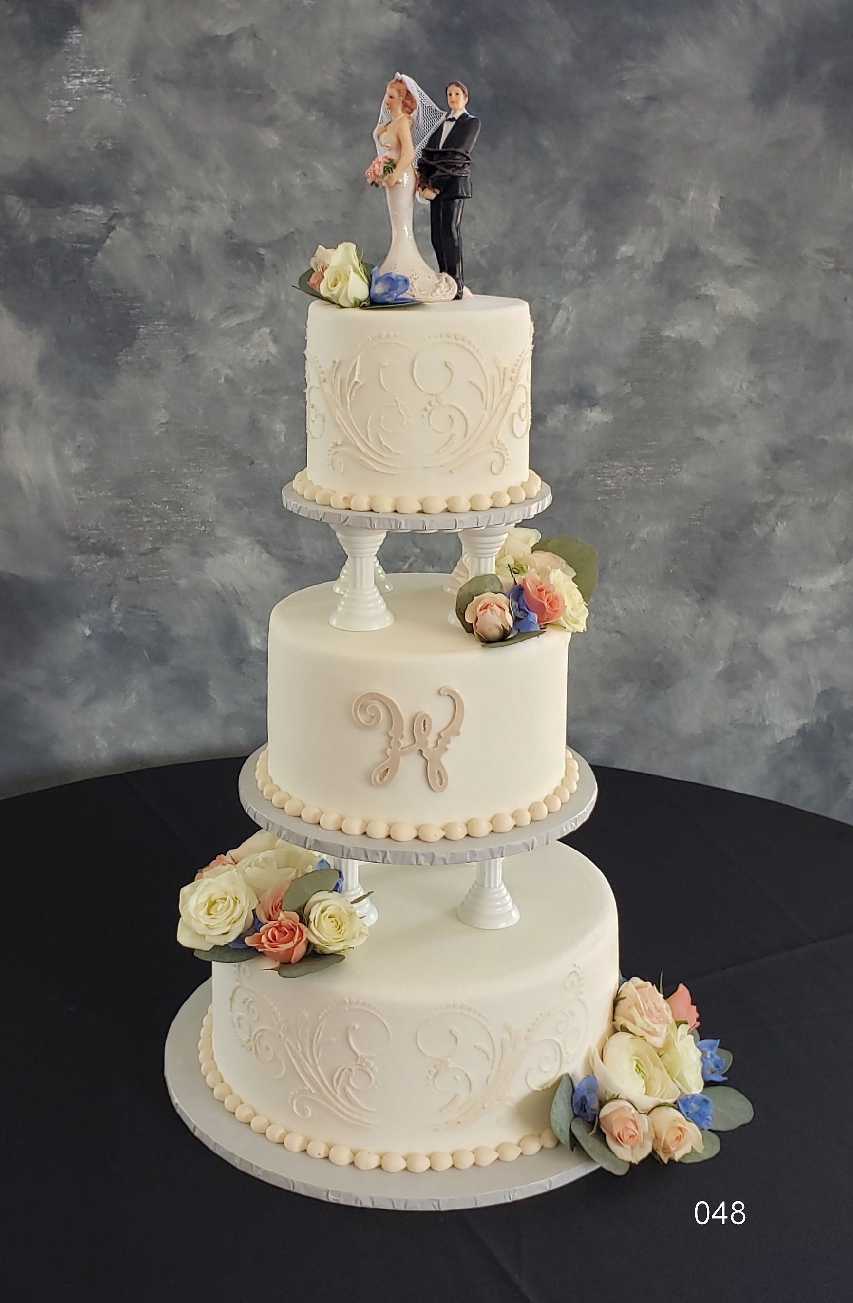 Three-tier white wedding cake with floral accents and a bride and groom topper