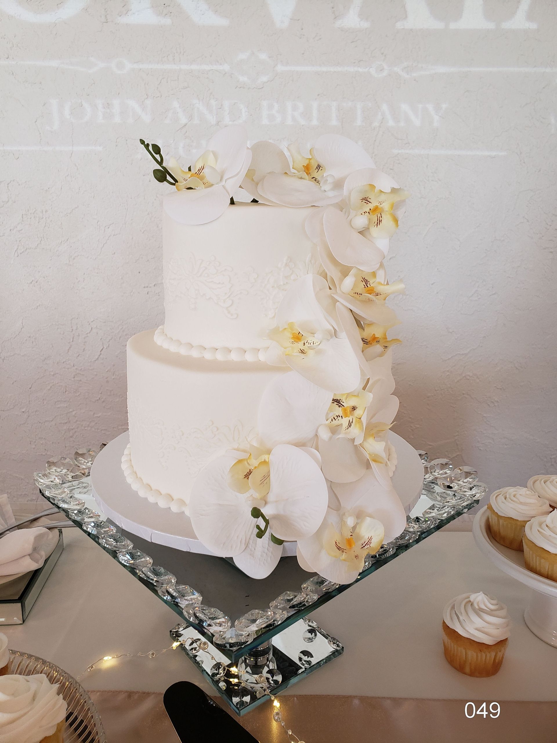 Two-tier white wedding cake with cascading white flowers on a mirrored stand
