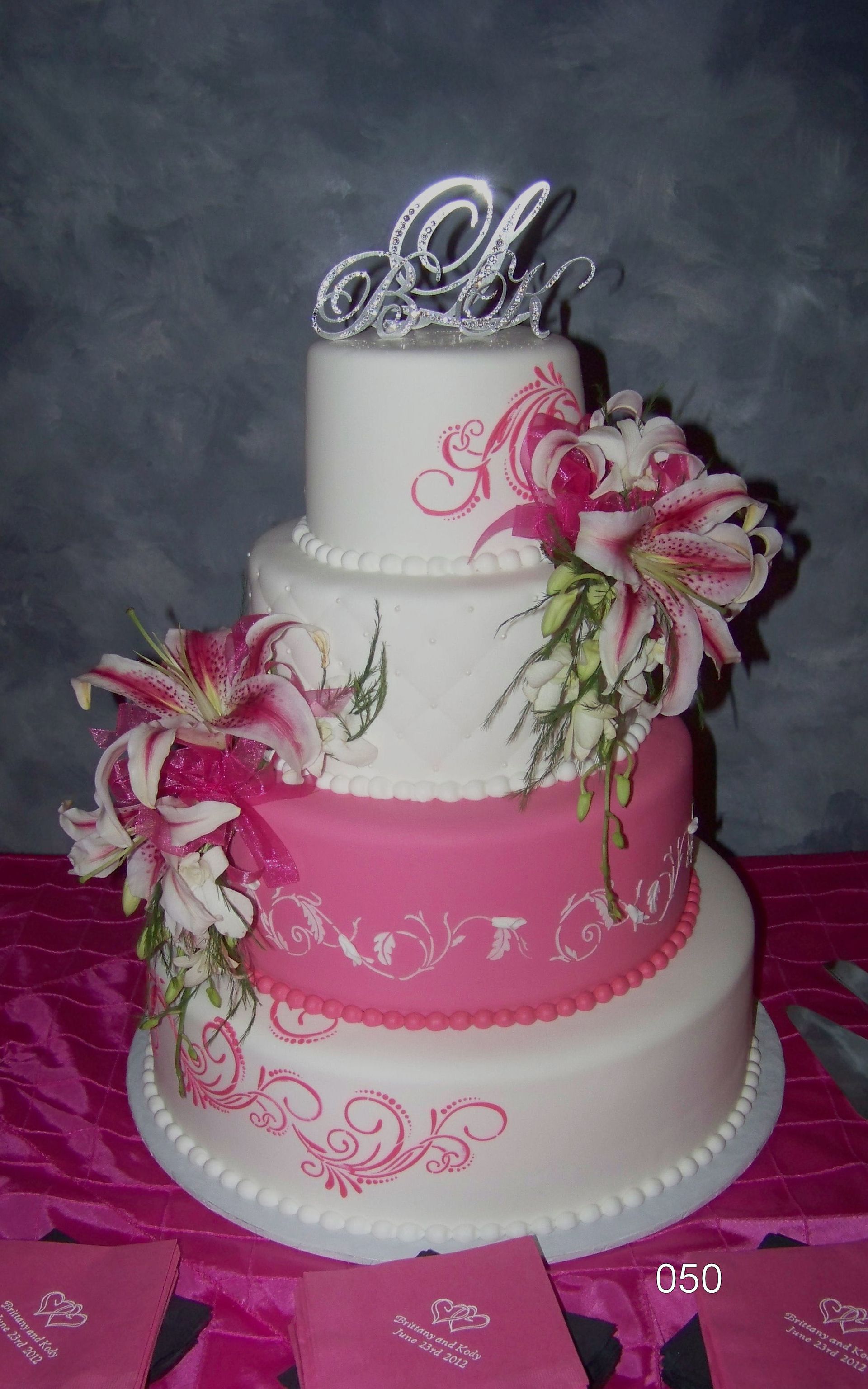Three-tier pink and white wedding cake with floral decorations and silver topper