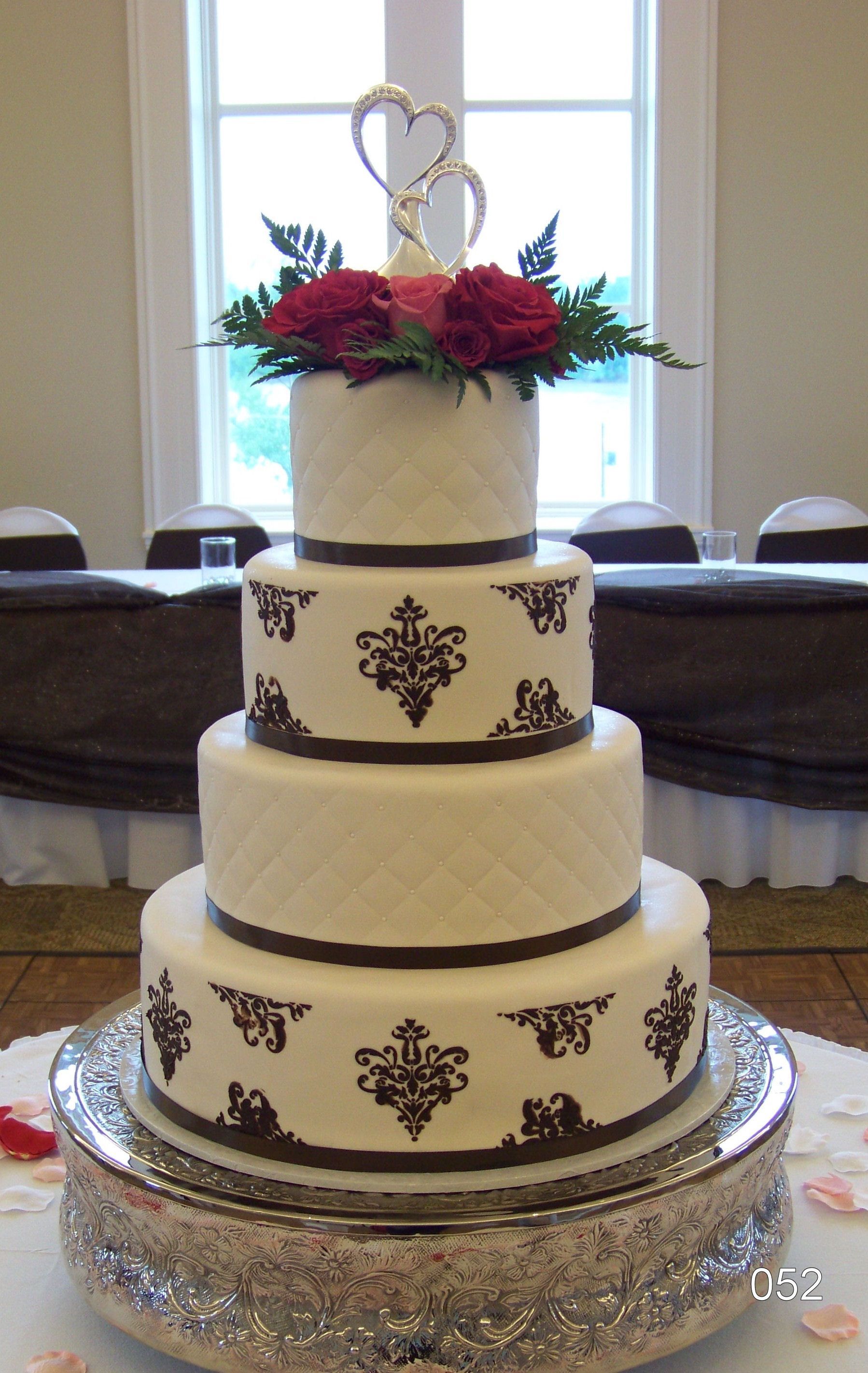 Three-tier white wedding cake with gold accents and red flowers on top in a banquet hall