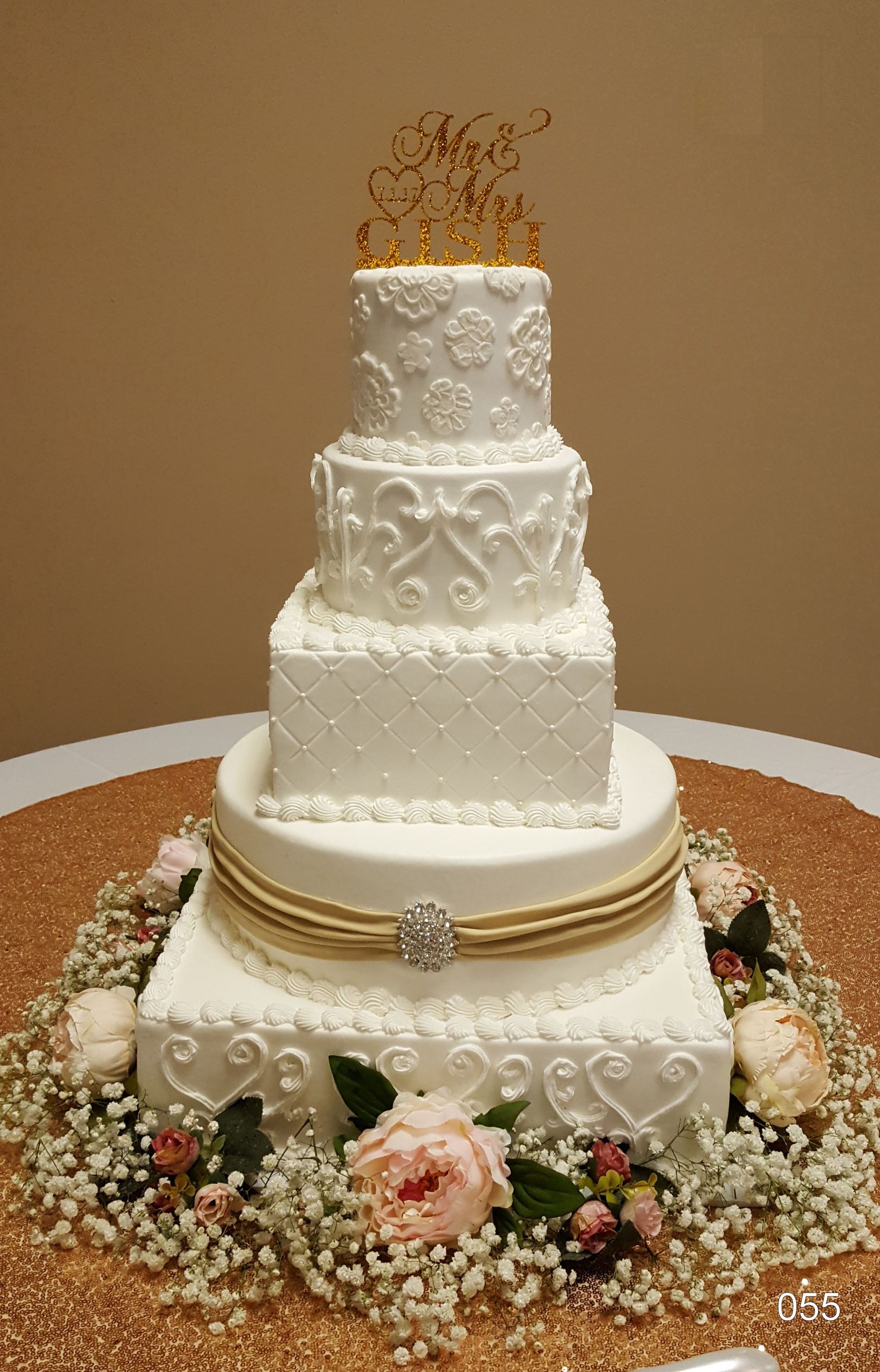 White tiered wedding cake with gold topper and floral base decoration