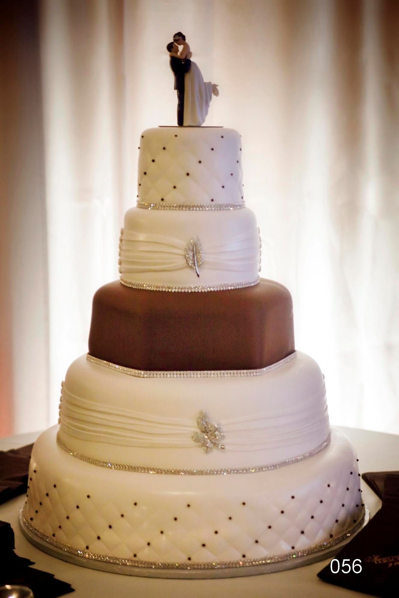 Four-tier wedding cake with white, brown, and speckled layers, topped by a bride and groom figurine