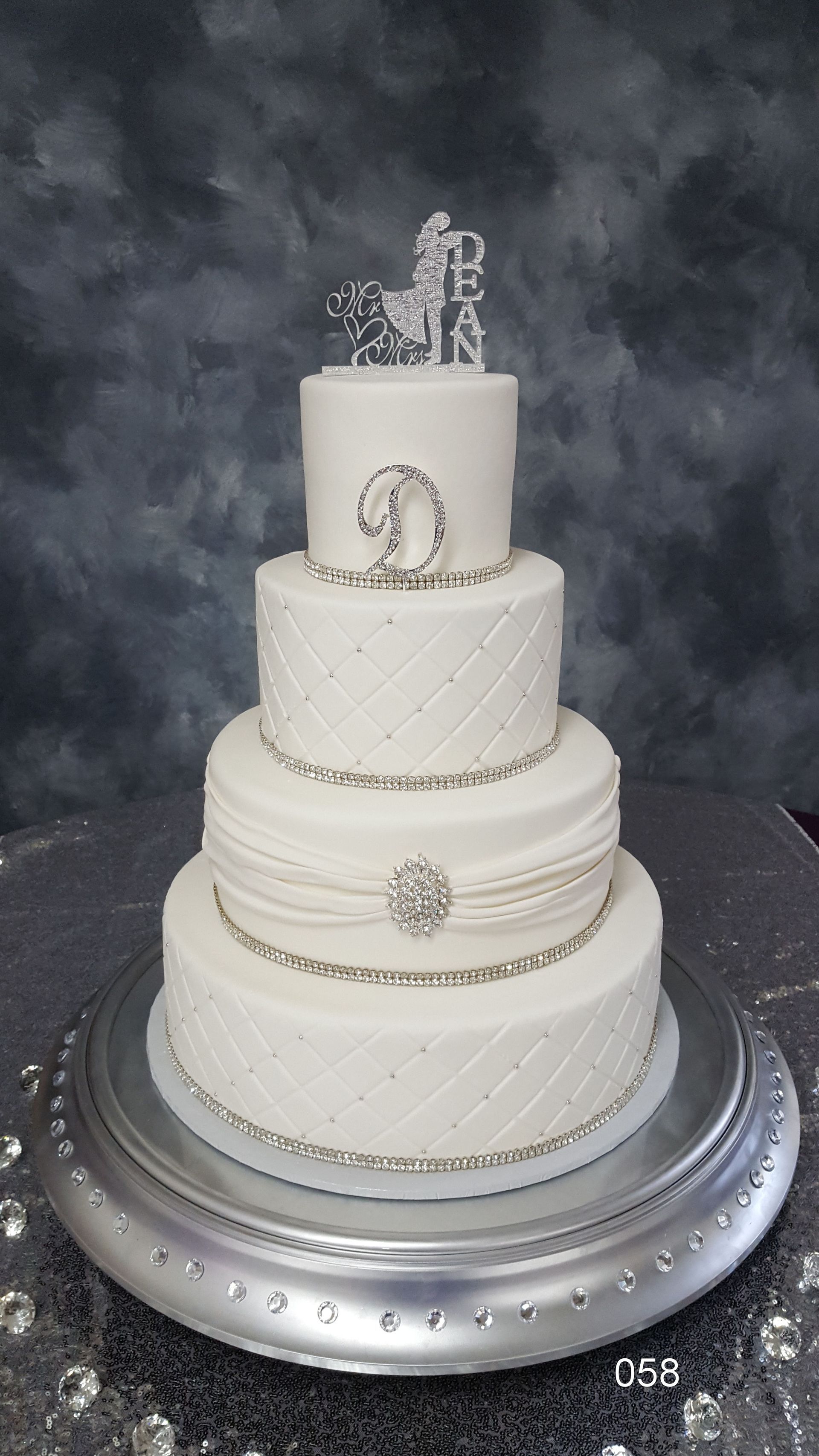 Elegant white tiered wedding cake with pearl and silver accents on a silver stand against a dark backdrop