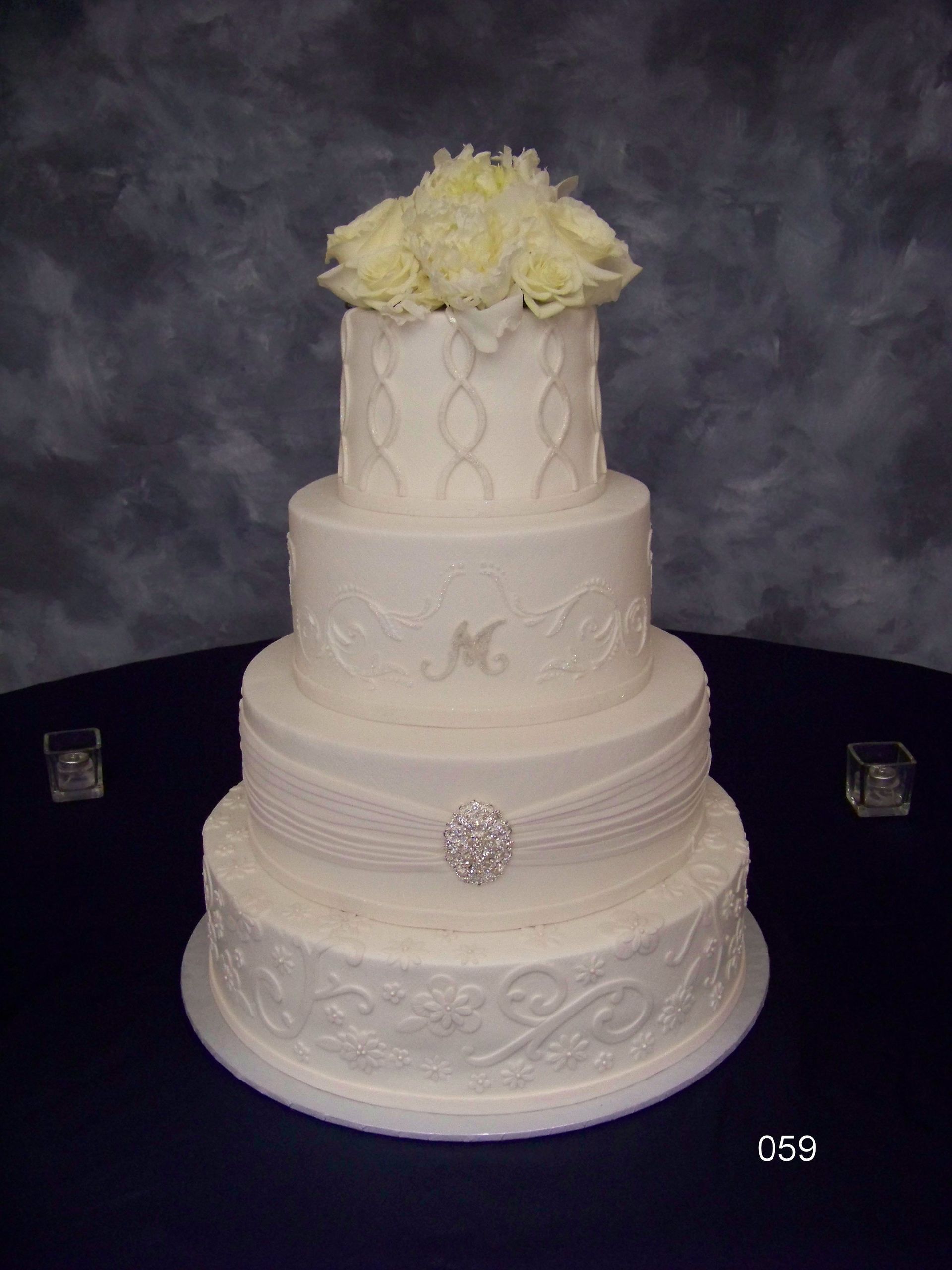 Elegant white tiered wedding cake with floral topper on a dark table backdrop