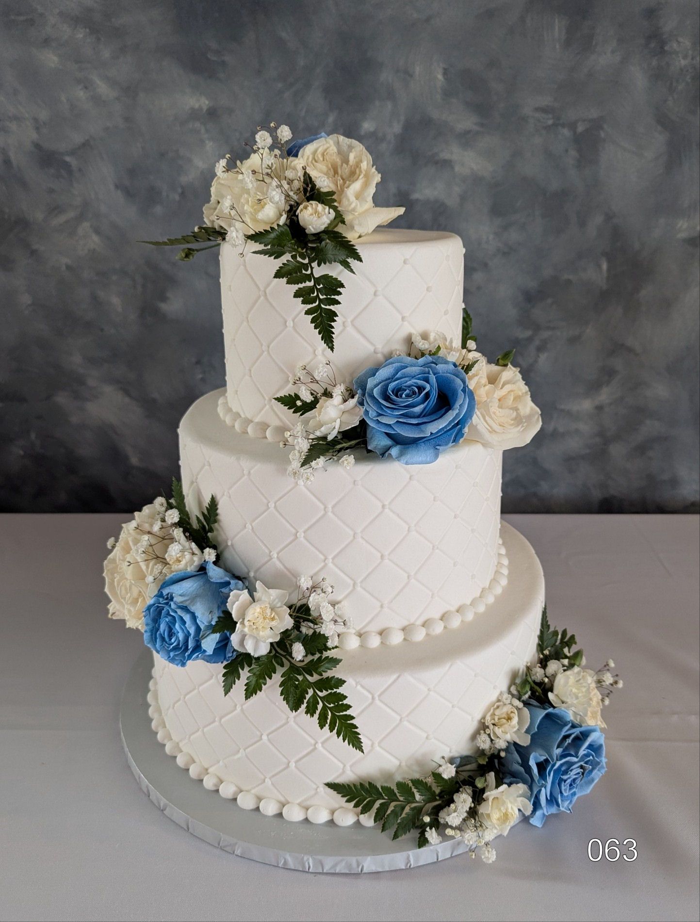 Three-tier white cake with blue and cream floral decorations