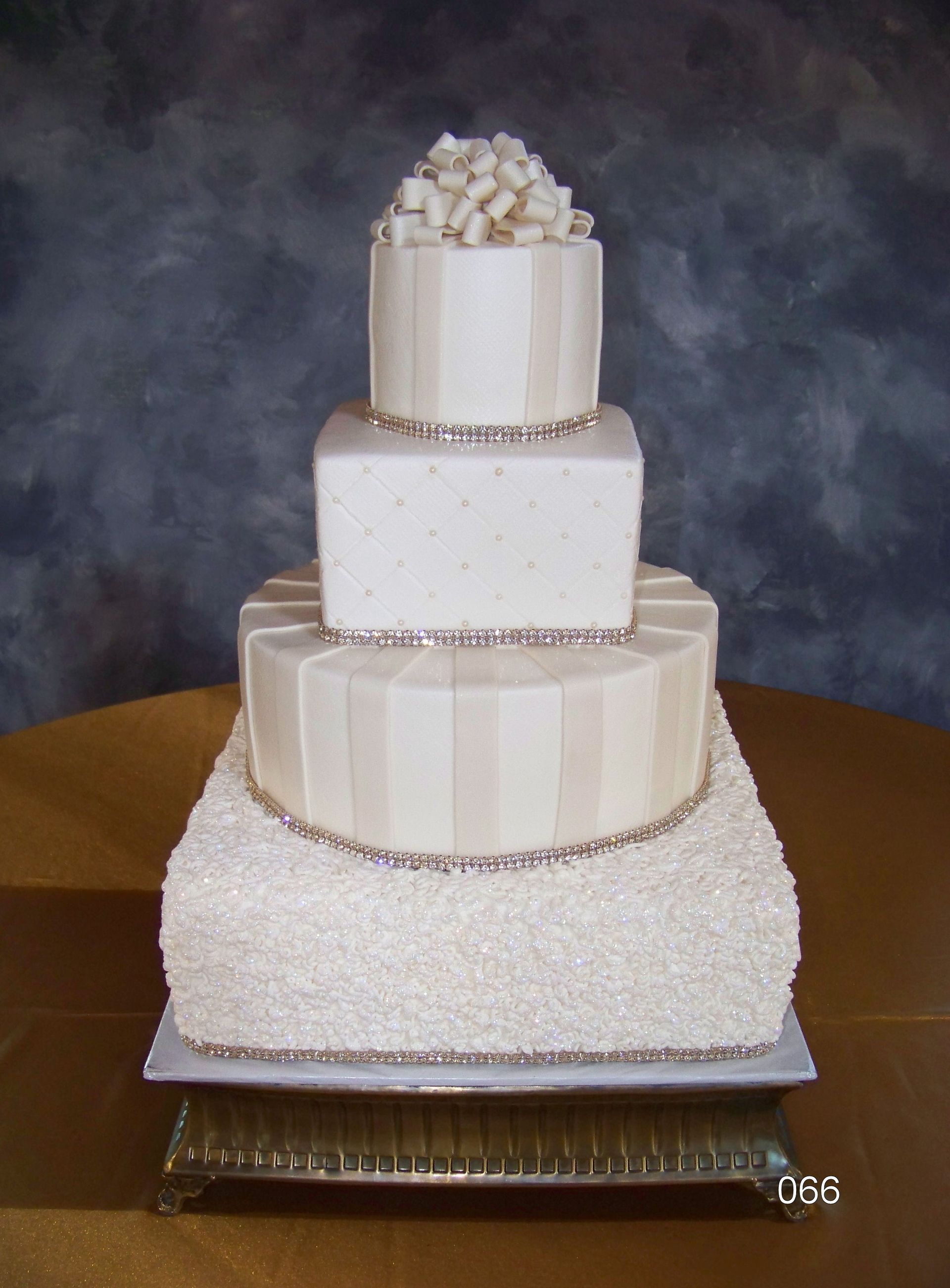 Four-tier white wedding cake with silver accents and a top layer of square marshmallow-like pieces