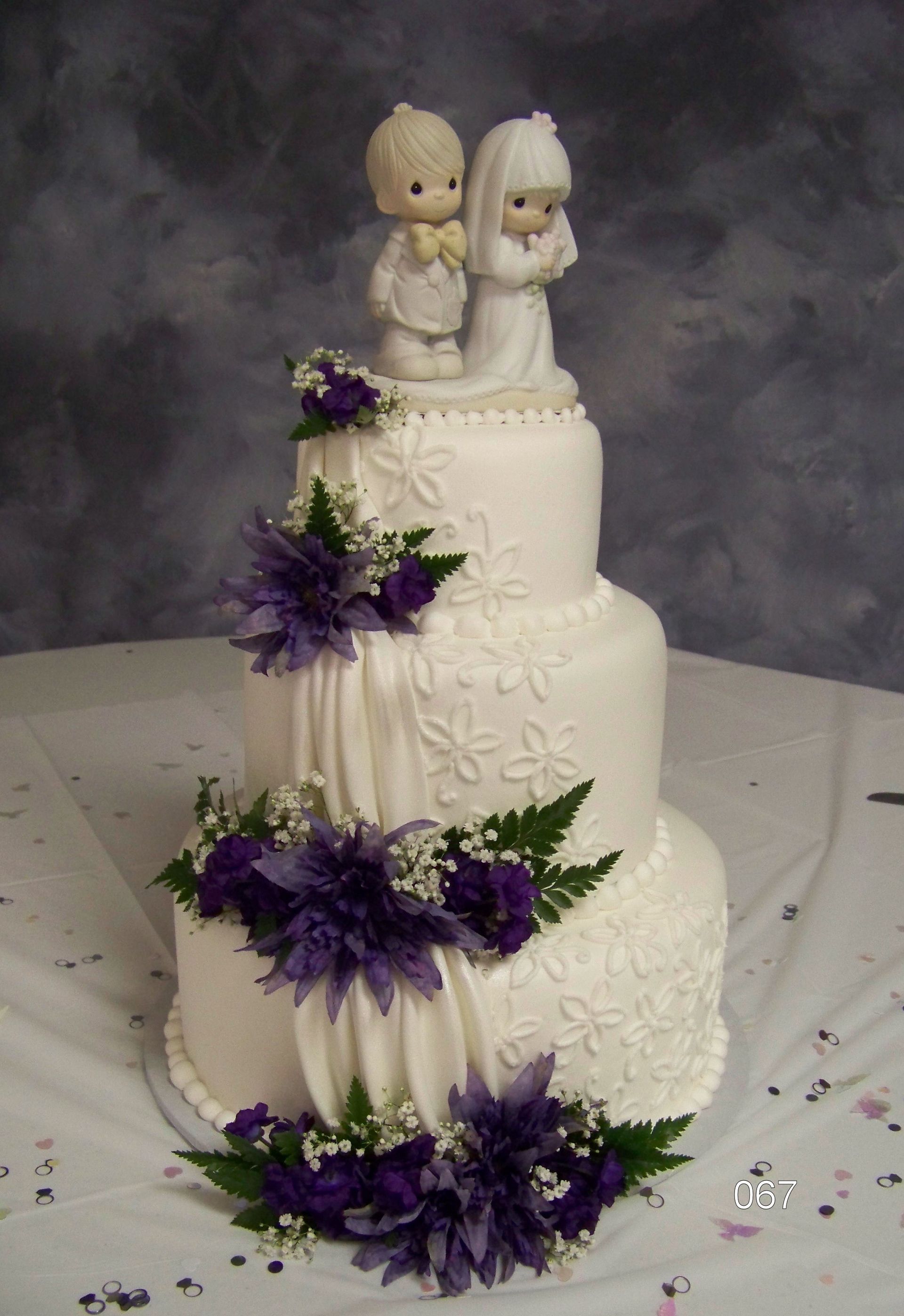 Three-tier white wedding cake with purple flowers and a bride-and-groom topper