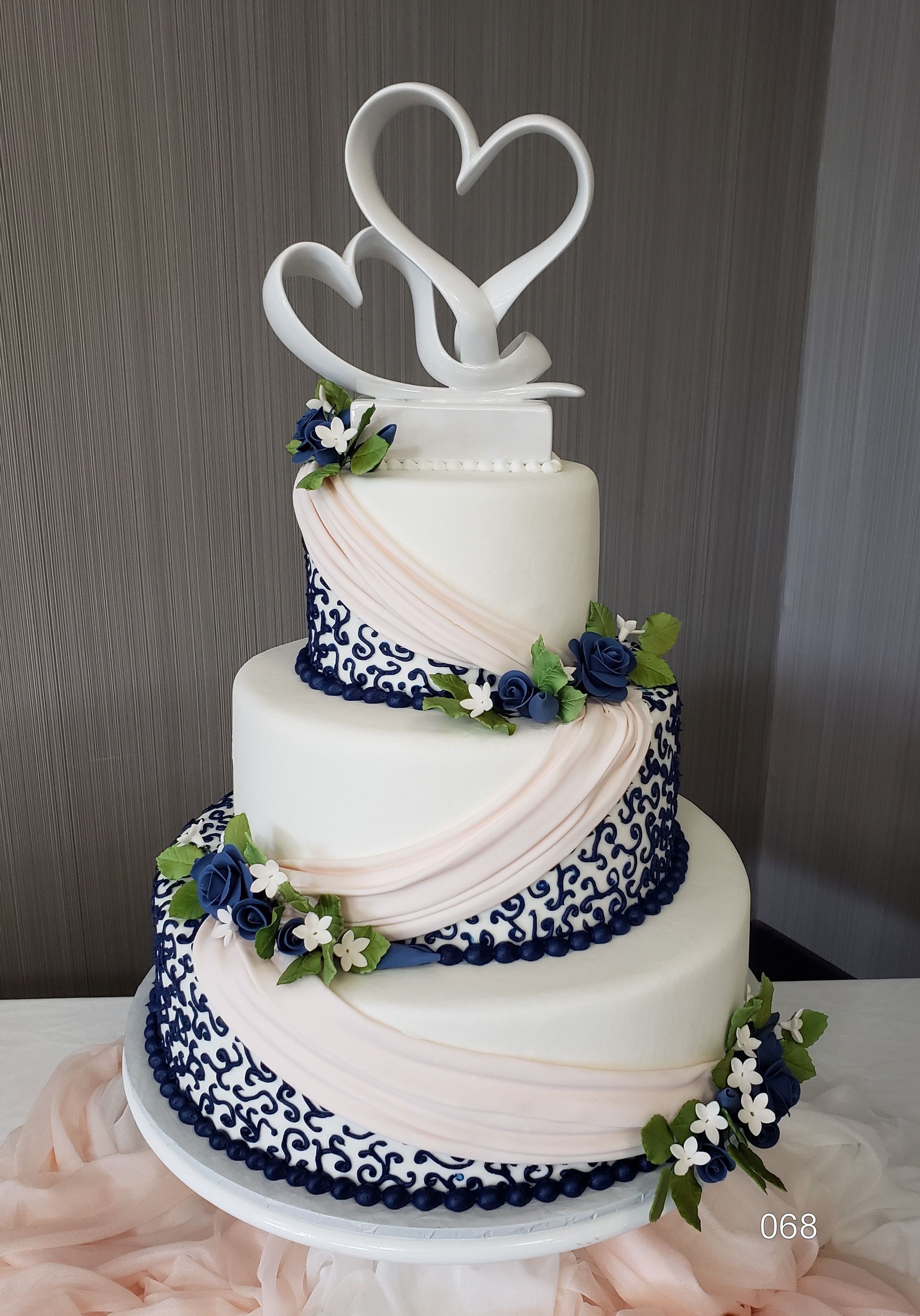 Three-tier white wedding cake with blue floral accents and heart topper