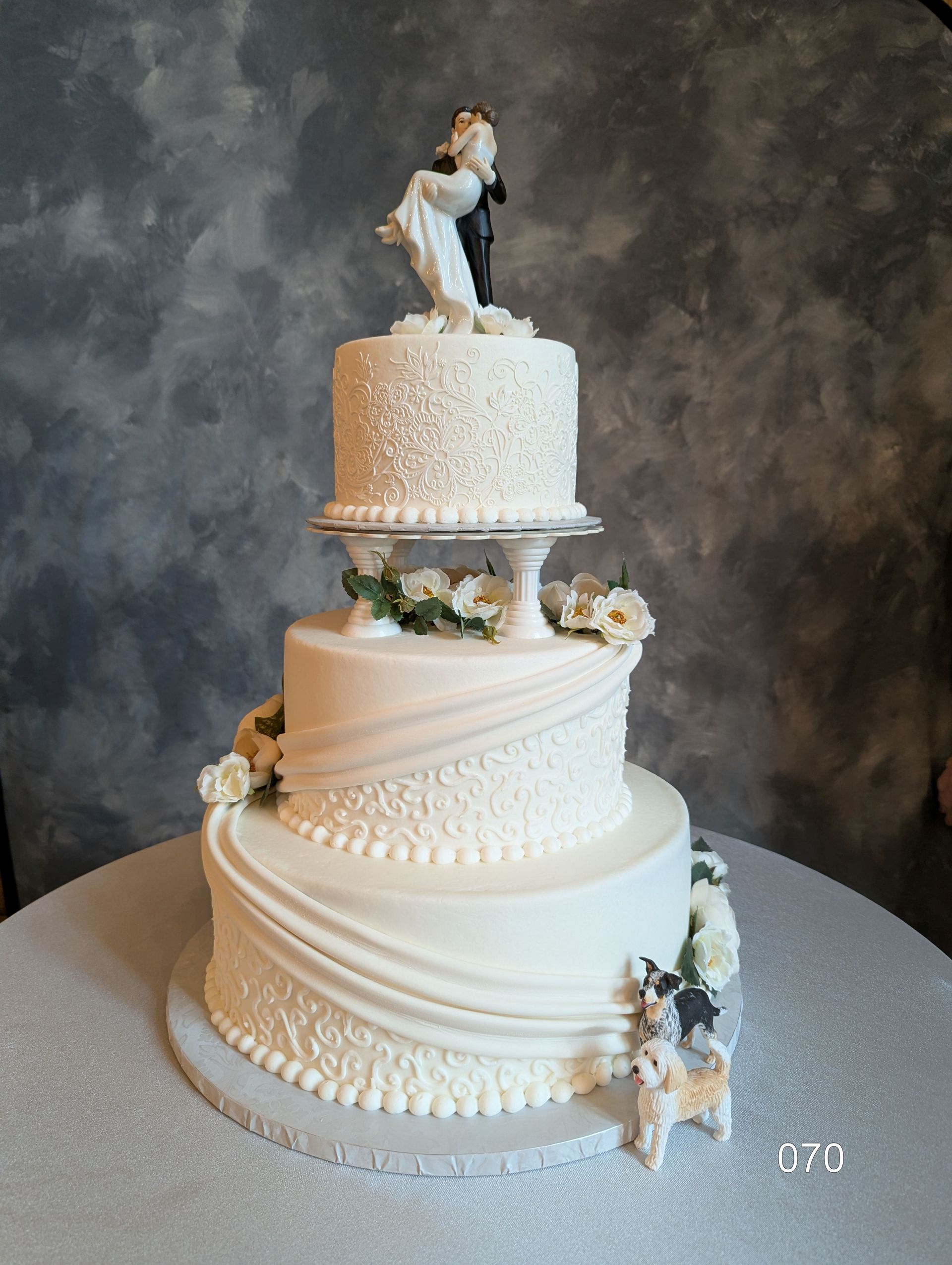 Three-tier white wedding cake with floral accents and a bride-and-groom topper