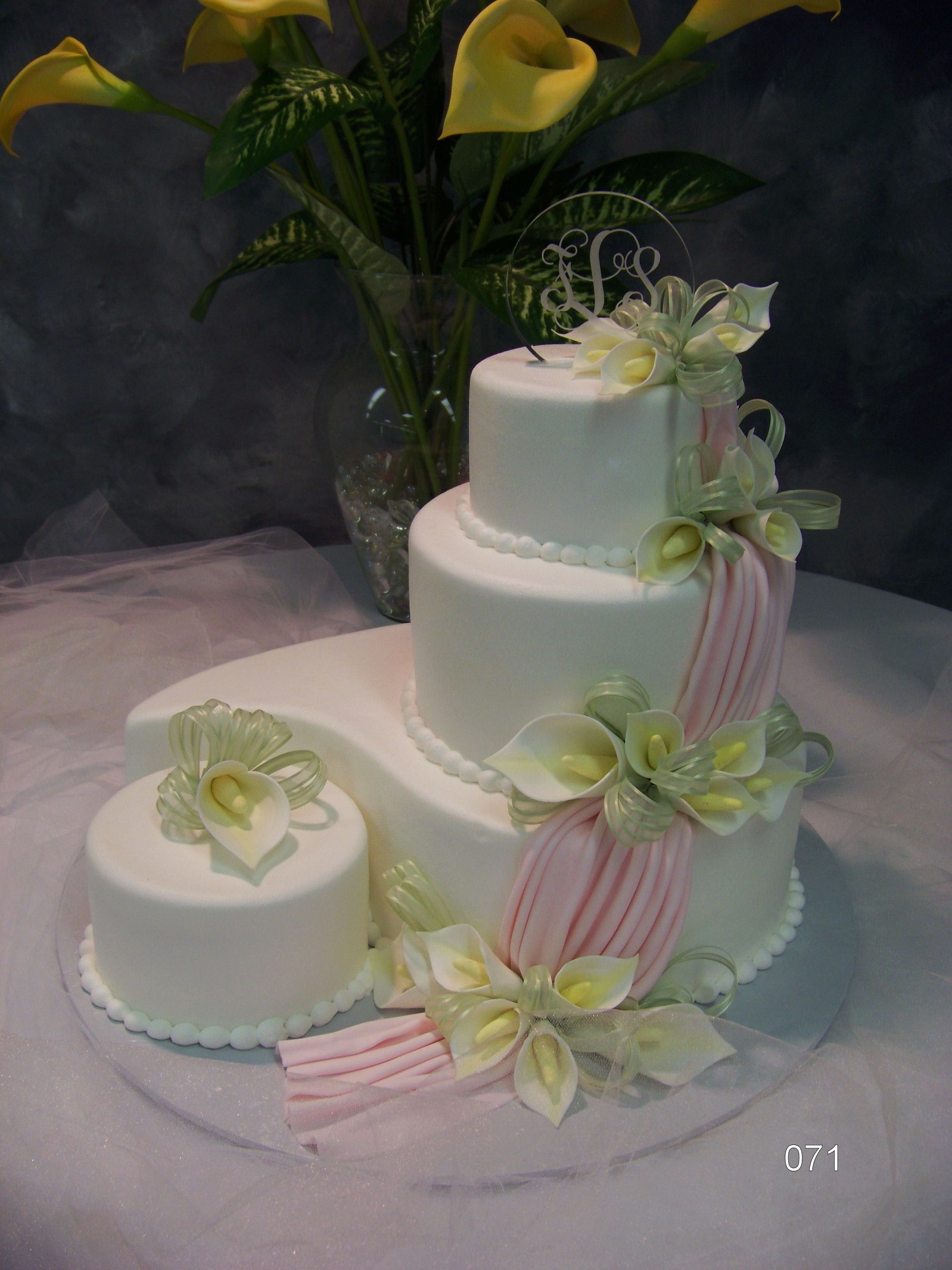 White three-tier cake with yellow and green floral decorations, beside a matching small cake on a table.