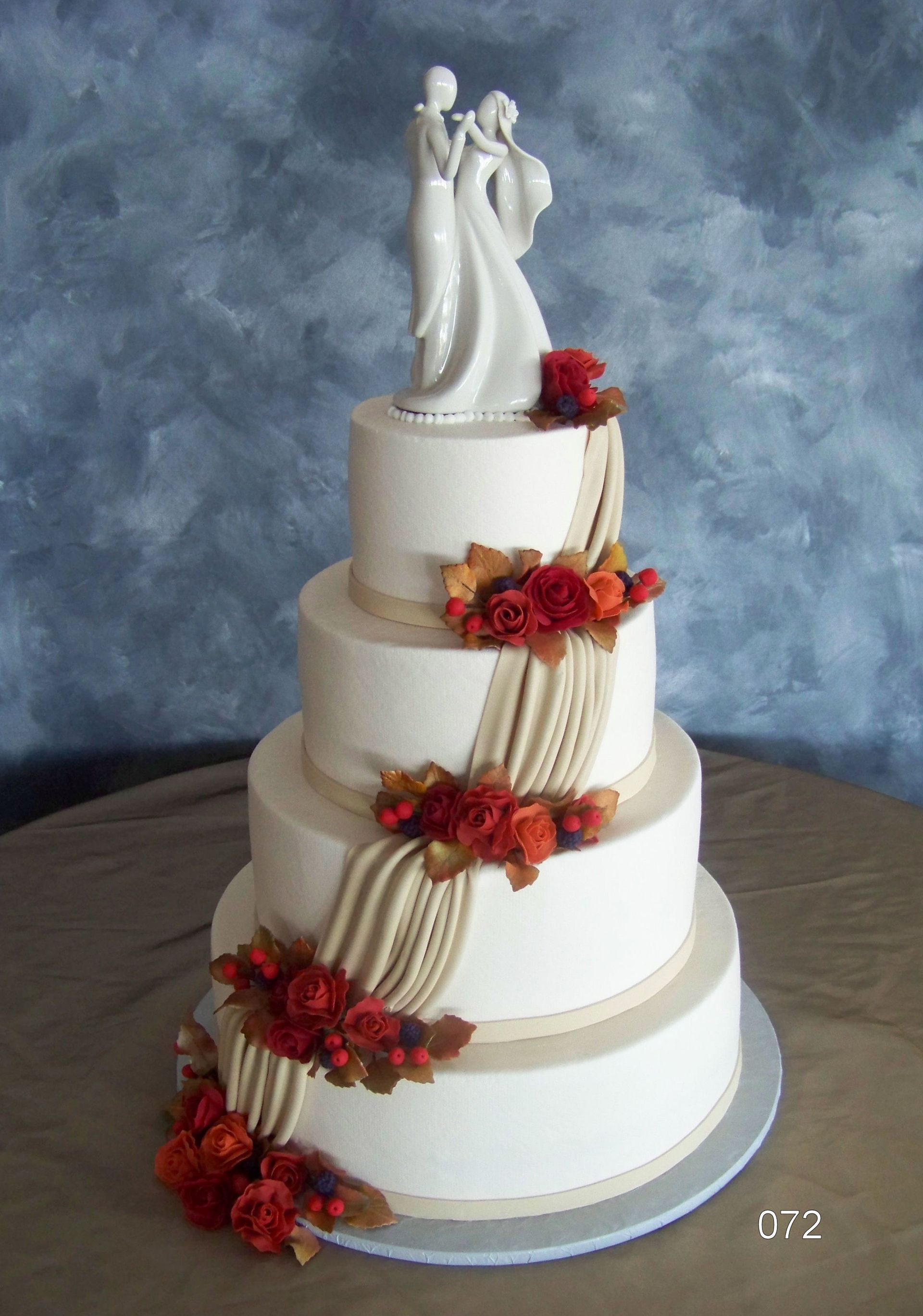 Four-tier white wedding cake with red flowers and bride-and-groom topper