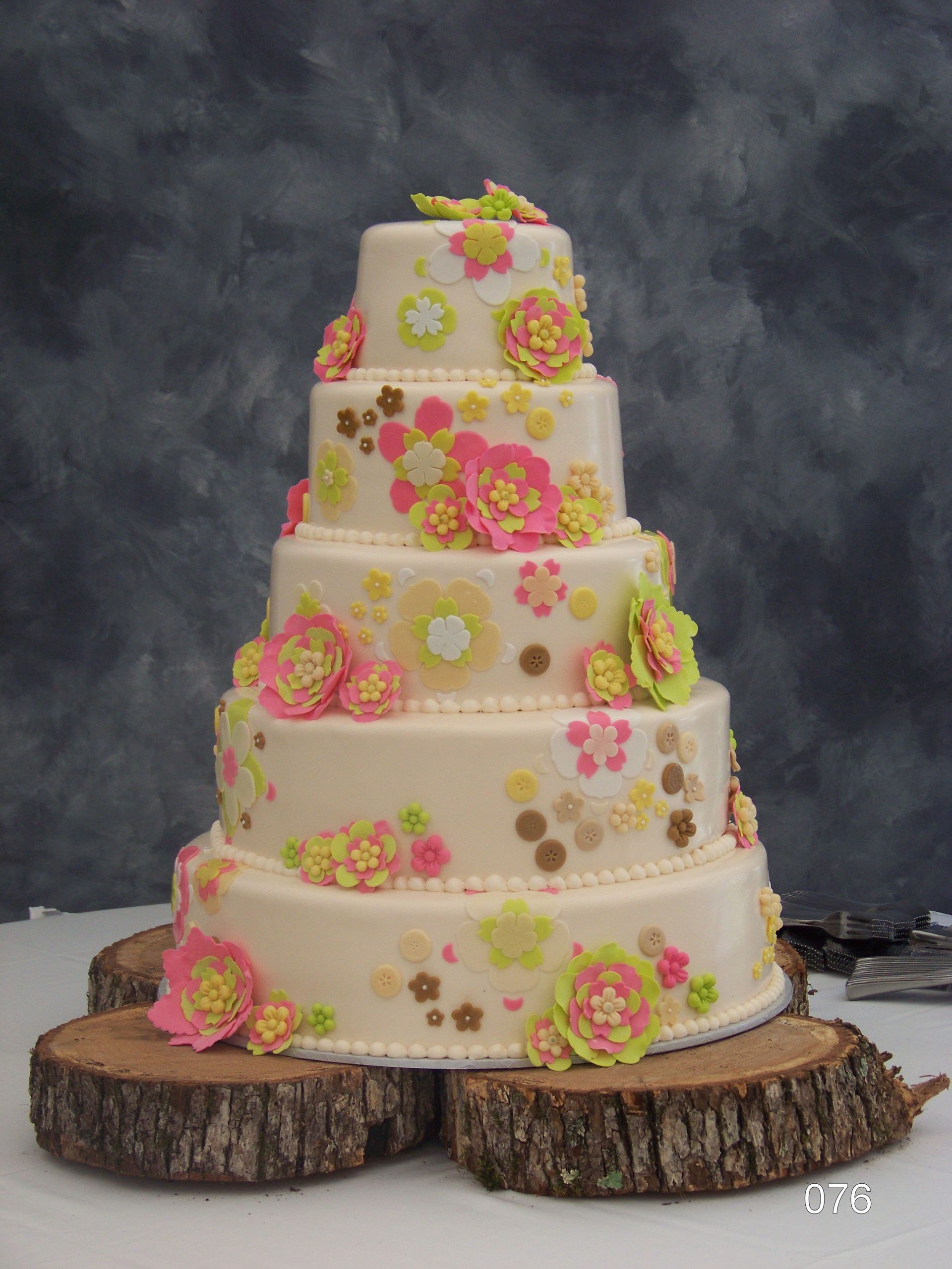 Tiered white wedding cake with pink and yellow floral decorations on rustic wood slices