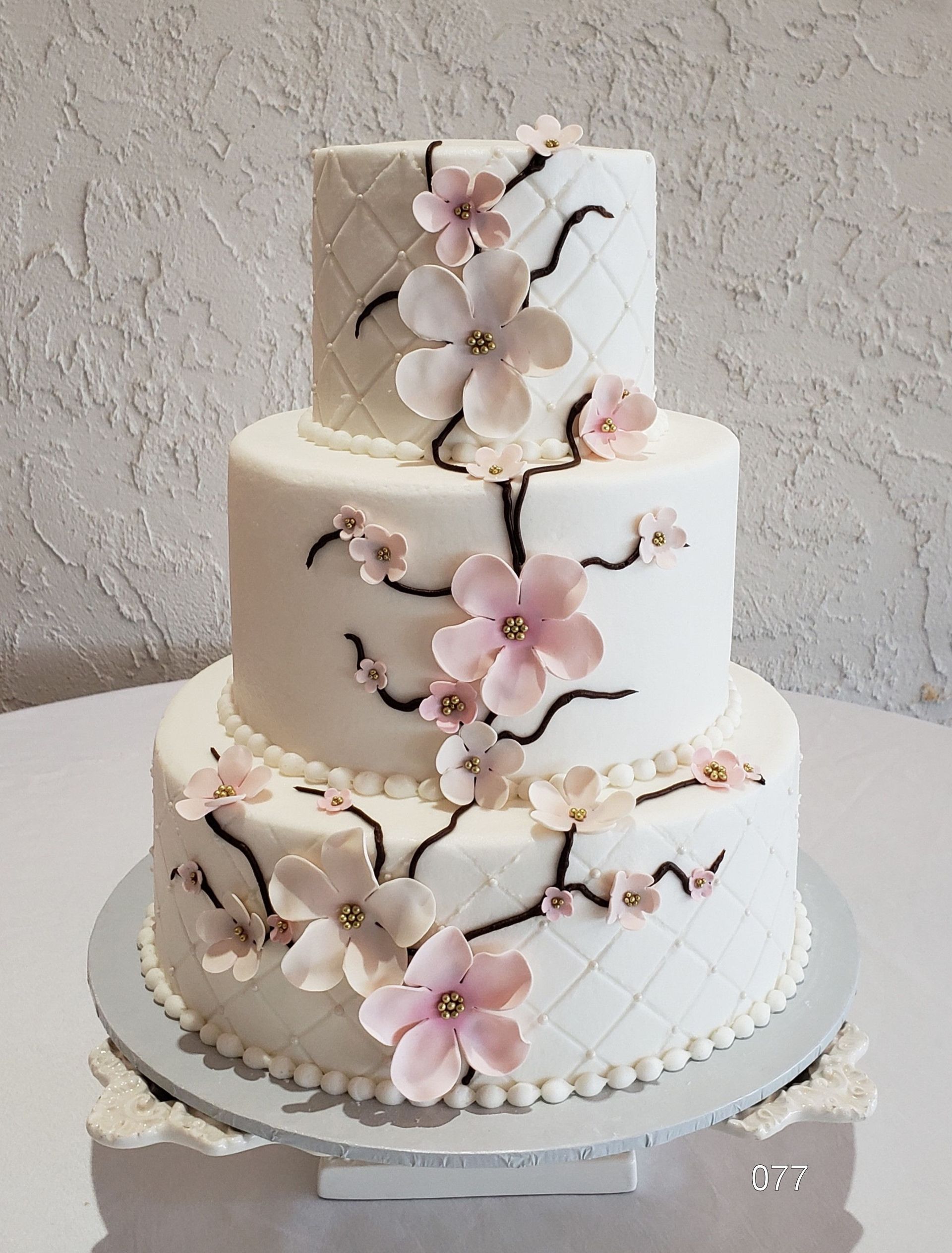 Two-tier white cake with pink cherry blossom decorations and a lattice pattern