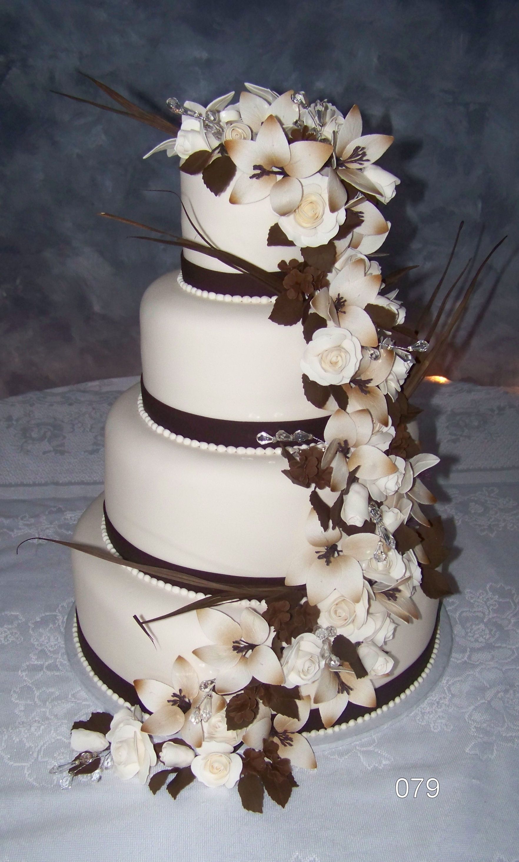 Three-tier white wedding cake with dark ribbon accents and cascading white and brown flowers