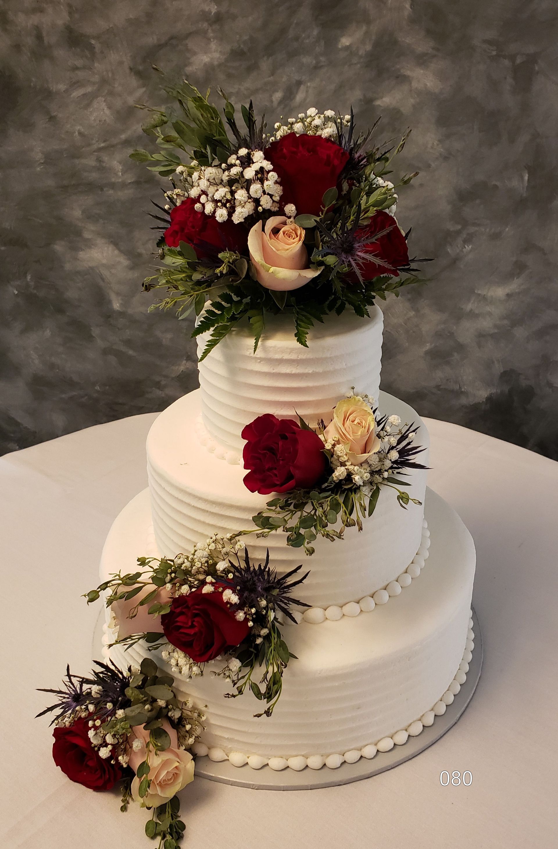 Three-tier white wedding cake with red and cream floral decorations and greenery