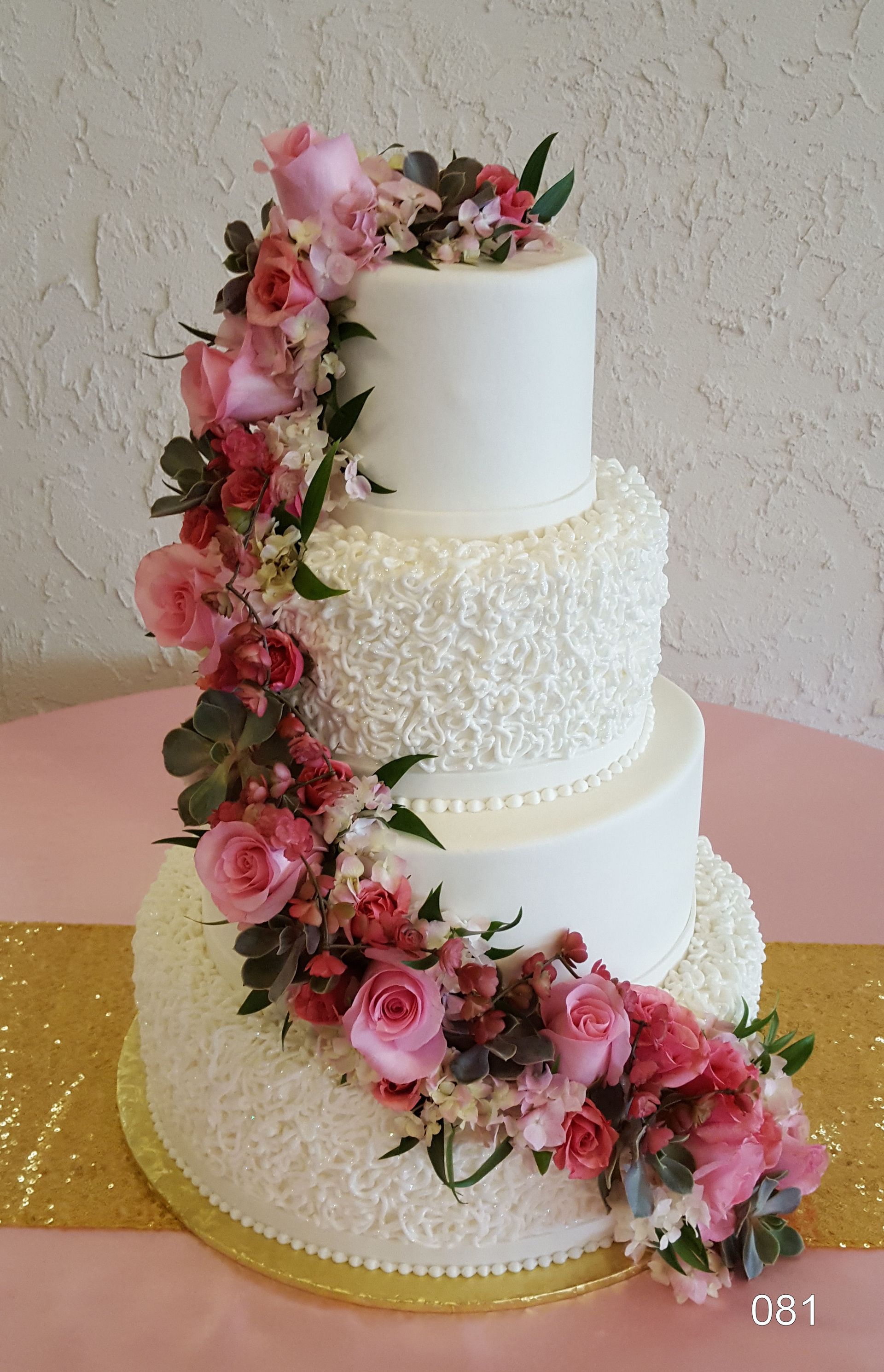 Three-tier white cake with pink roses and greenery cascading down the side
