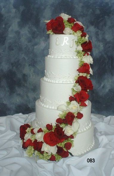 Four-tier white wedding cake with red and white roses cascading down the side