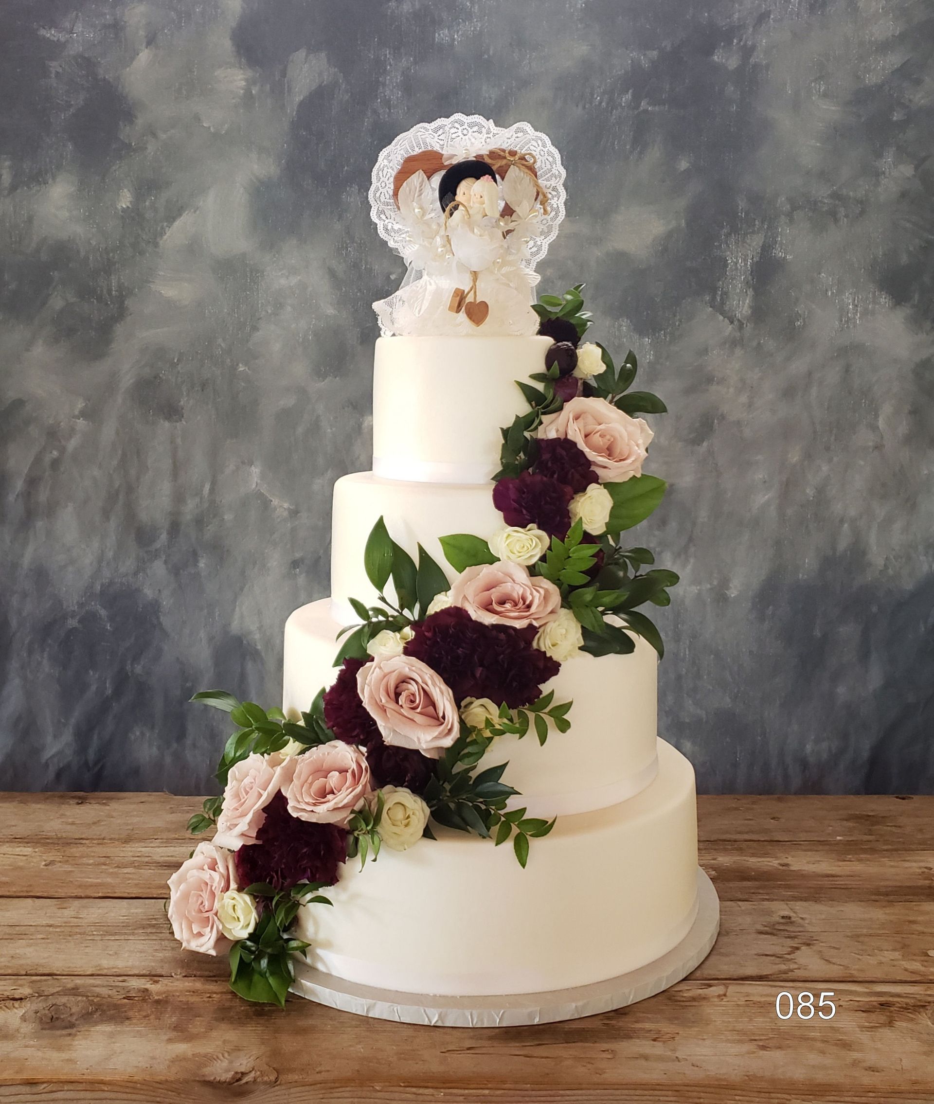 Three-tier white wedding cake with cascading pink and burgundy flowers and a jeweled topper